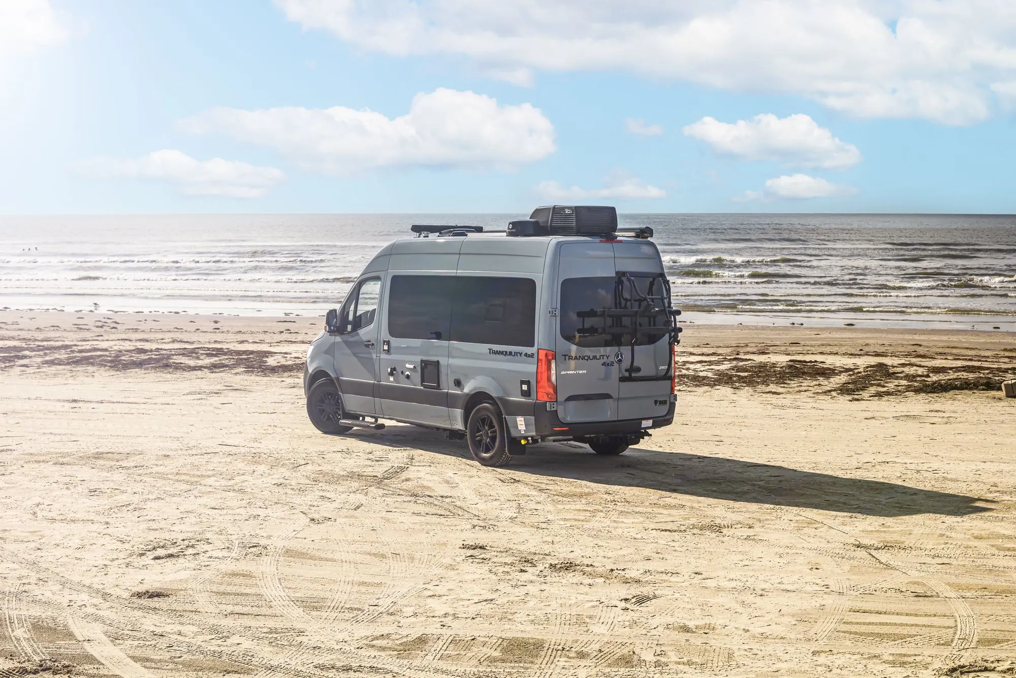 Gray Tranquility Sprinter RV rental on a sandy beach, ocean waves in background.. Thor Tranquility 2023