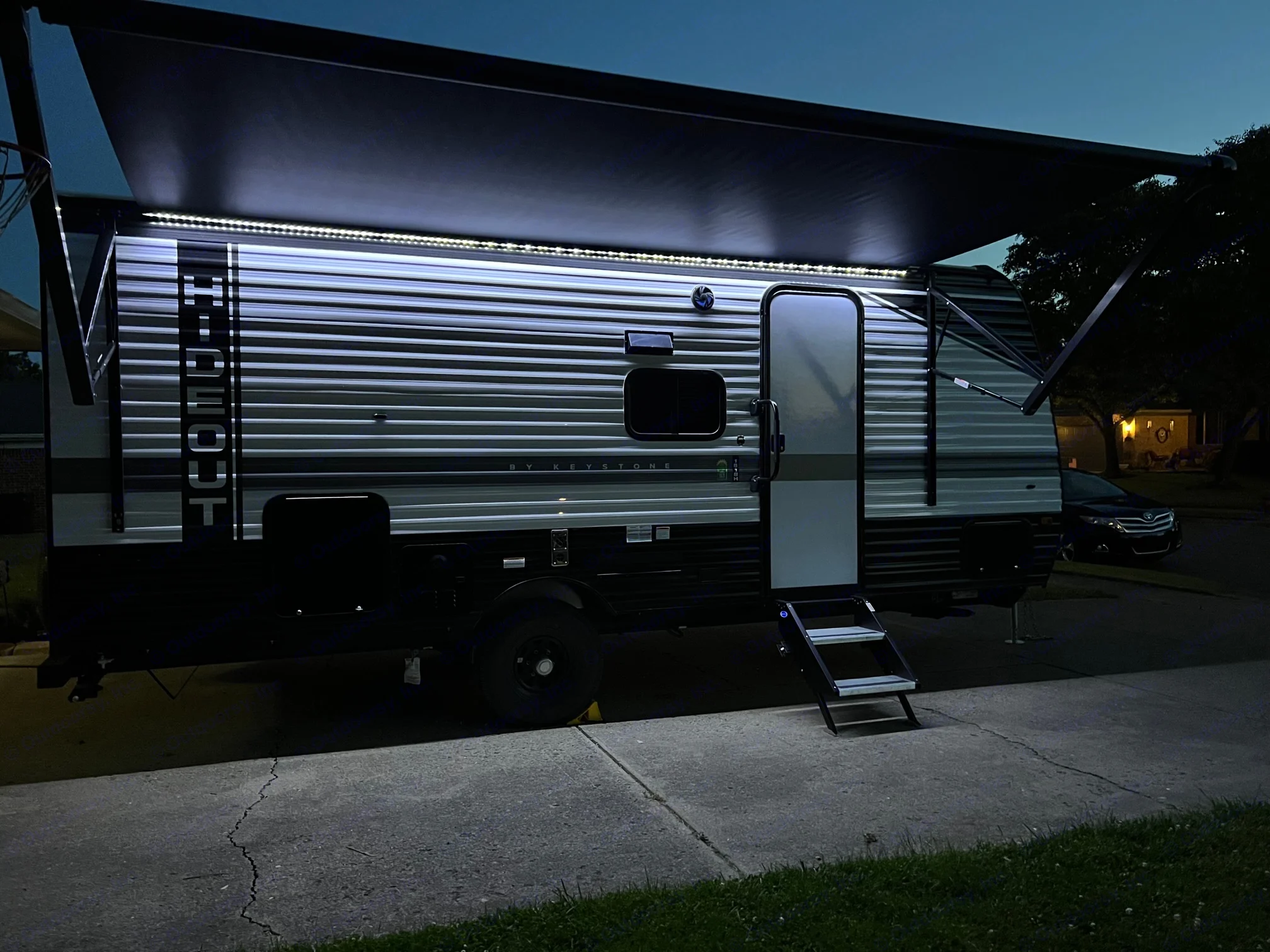 This travel trailer RV rental, with its bright LED awning lights and extended steps, is ready for adventure at night.. Hideout 181BH 2023