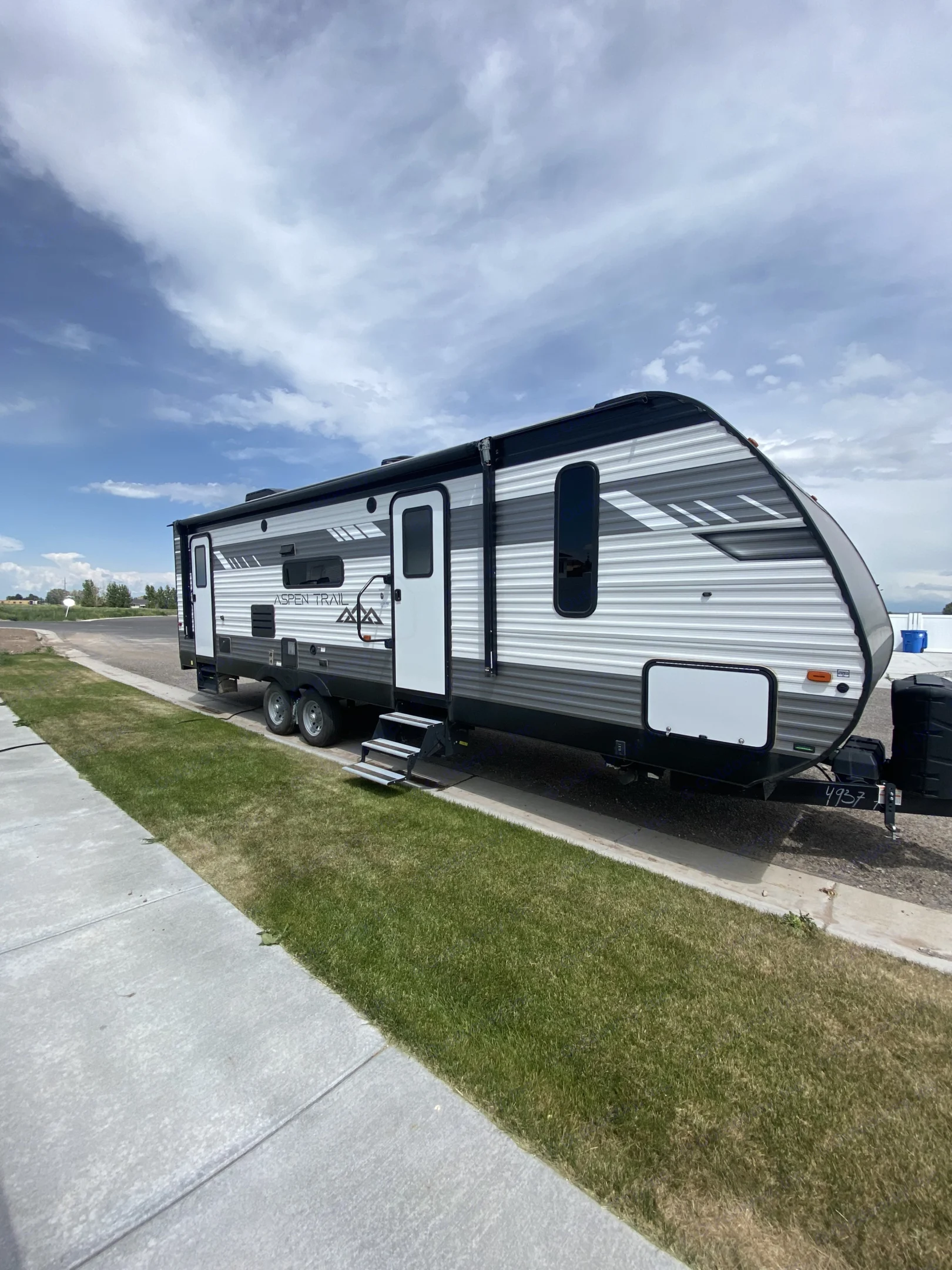 New Aspen Trail RV rental, gray and white, parked on an asphalt lot with steps down to grass.. Aspen Trail Aspen Trail Trailer 2021