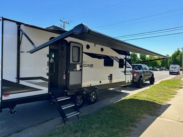 Sunny day view of an RV rental travel trailer with awning extended, hitched to a pickup. Imagine 2600RB 2023