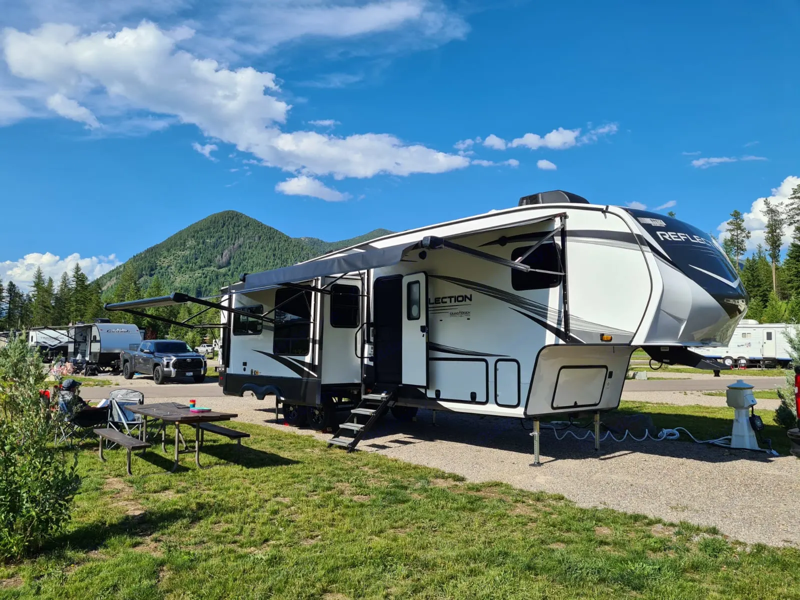 Spacious fifth-wheel RV, perfect for your next rv rental adventure, set up at a scenic mountain campground on a sunny day.. Grand Design Reflection 2023
