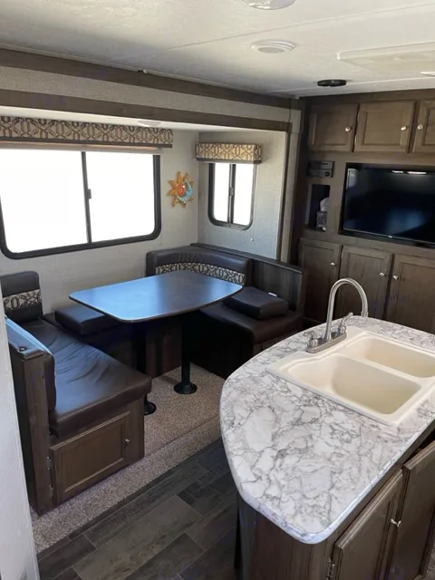 RV rental interior: kitchen with double sink, wood cabinets, TV, and dinette seating. Ready for adventures!. Keystone RV Bullet Ultra Lite 2018