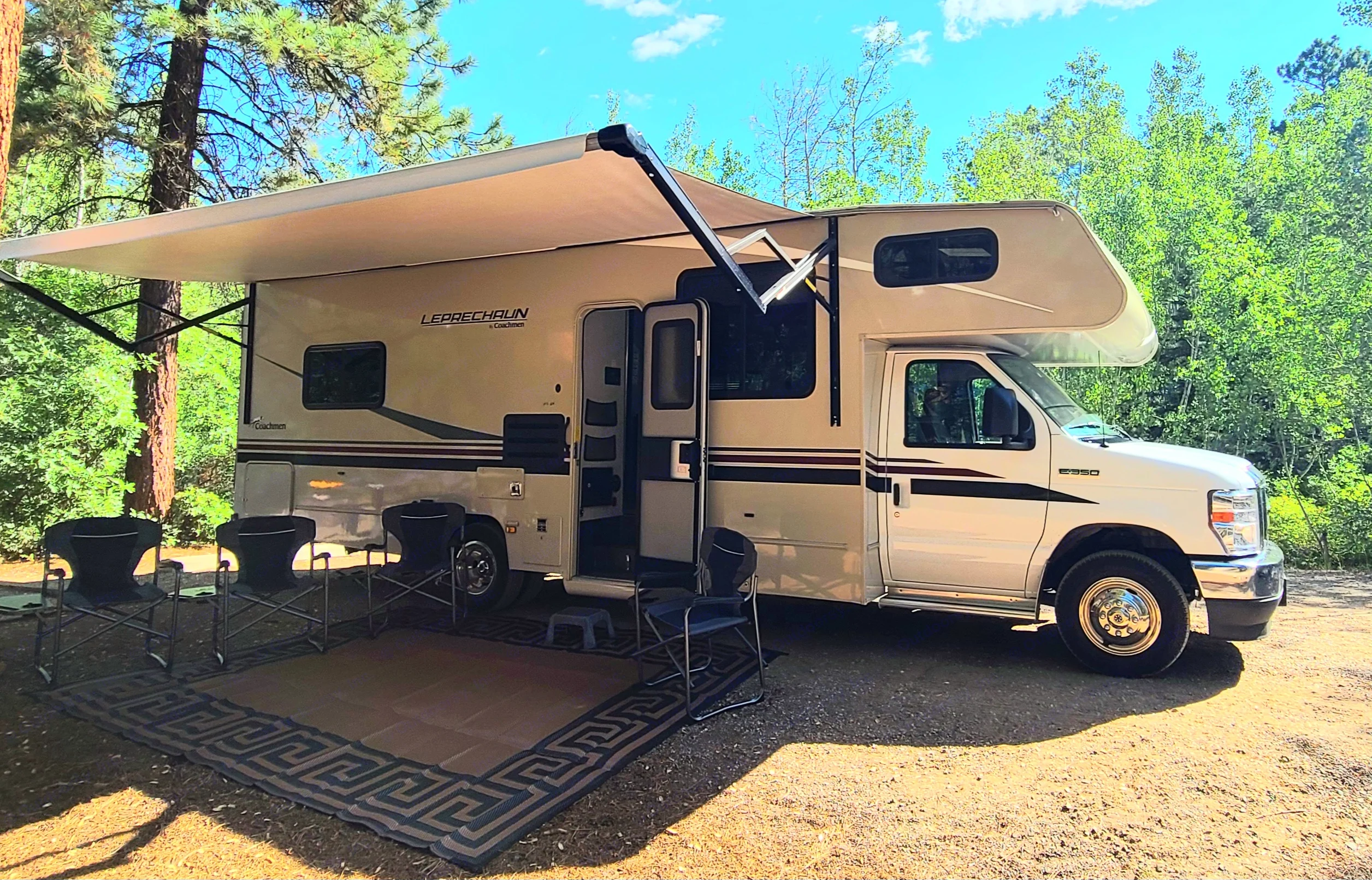 Coachmen Leprechaun RV rental: A Class C RV with an extended awning, outdoor rug, and chairs for a relaxing camp setup.. Coachman Leprechaun 2022