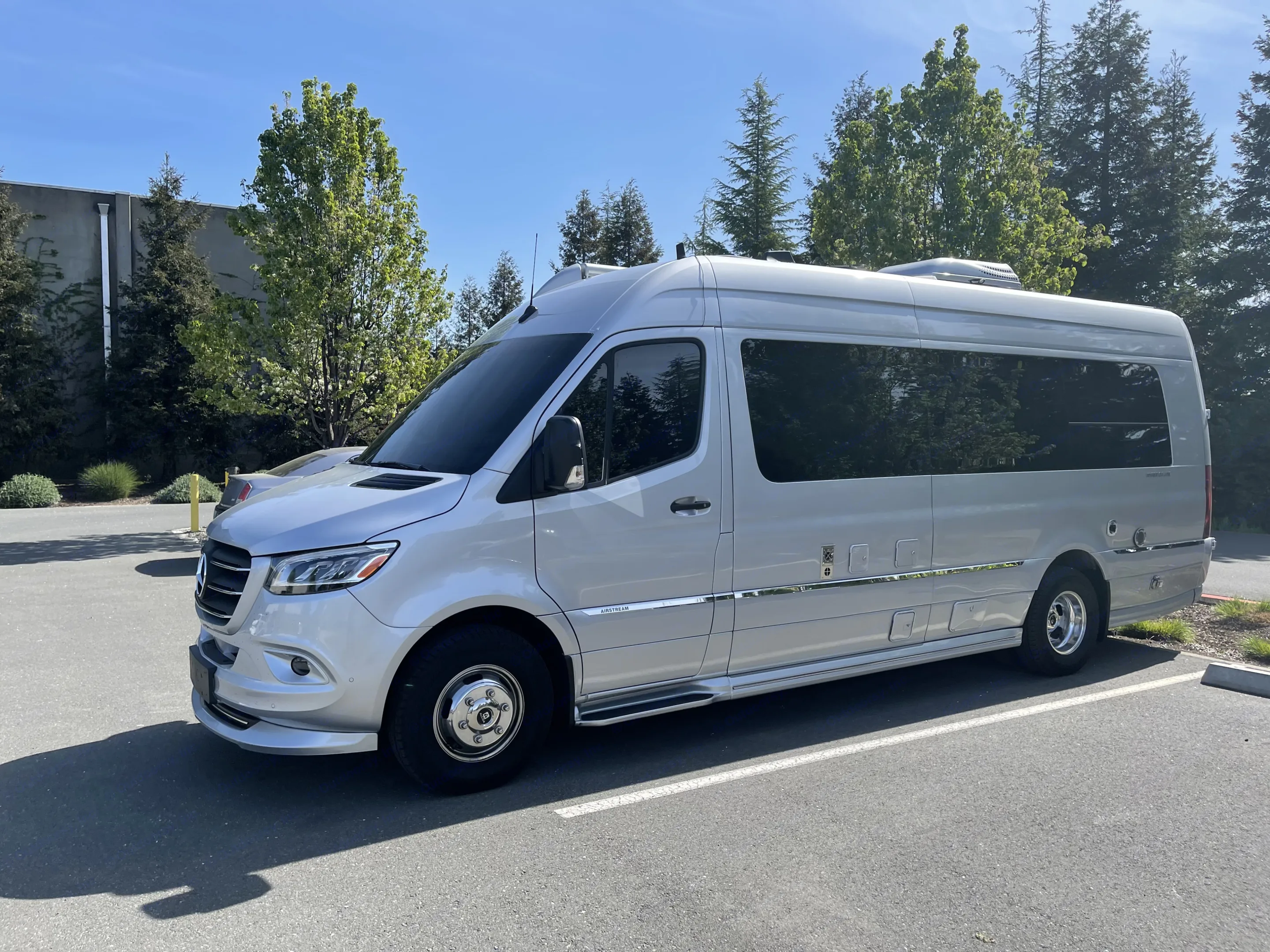 An RV rental's side, revealing exterior storage compartments (one open), a water fill, and sleek graphic stripes on a Ford E-350 base.. Airstream Interstate 2021