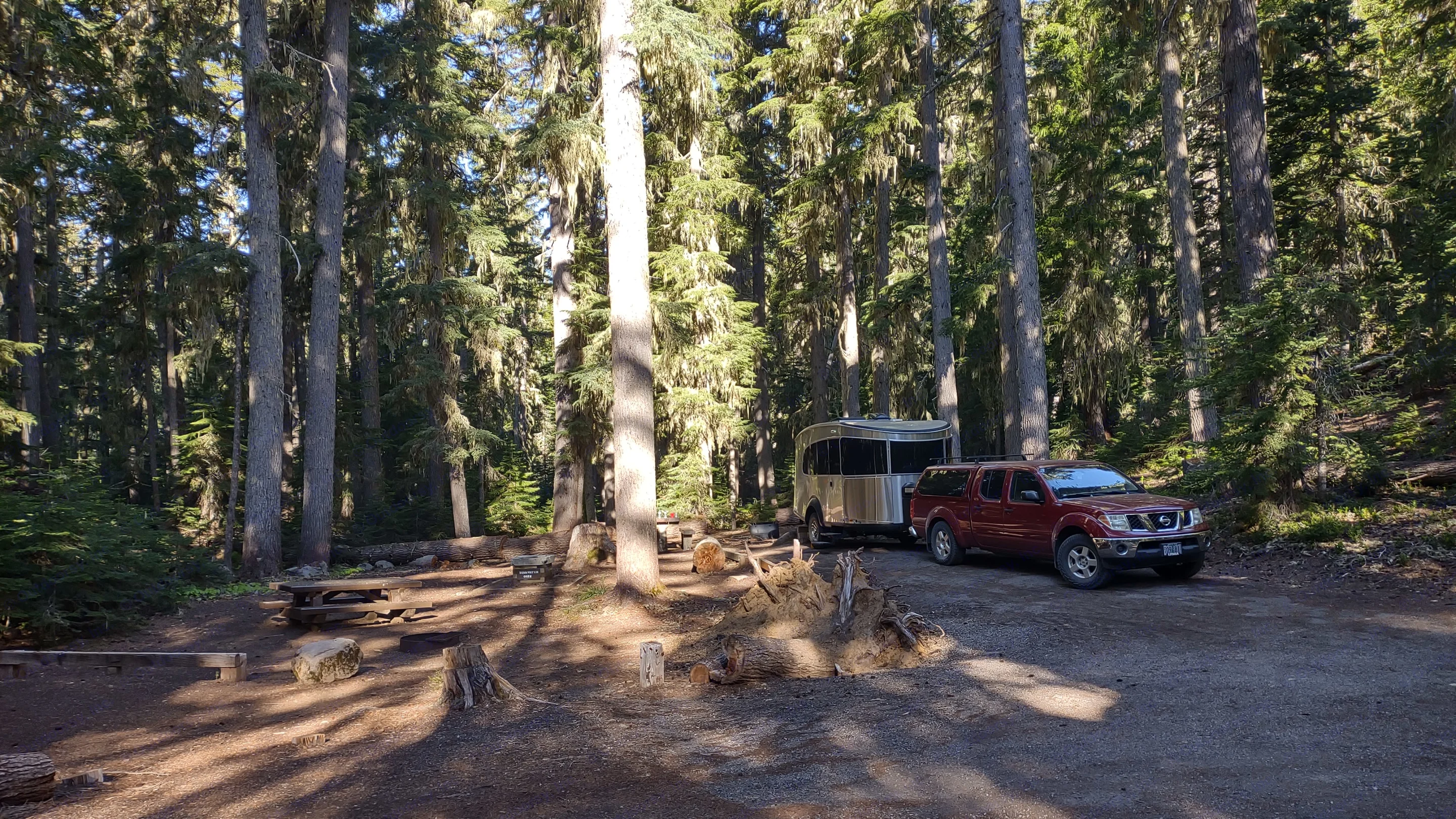 Forest campsite featuring a red pickup truck and a sleek. Airstream Basecamp 2022