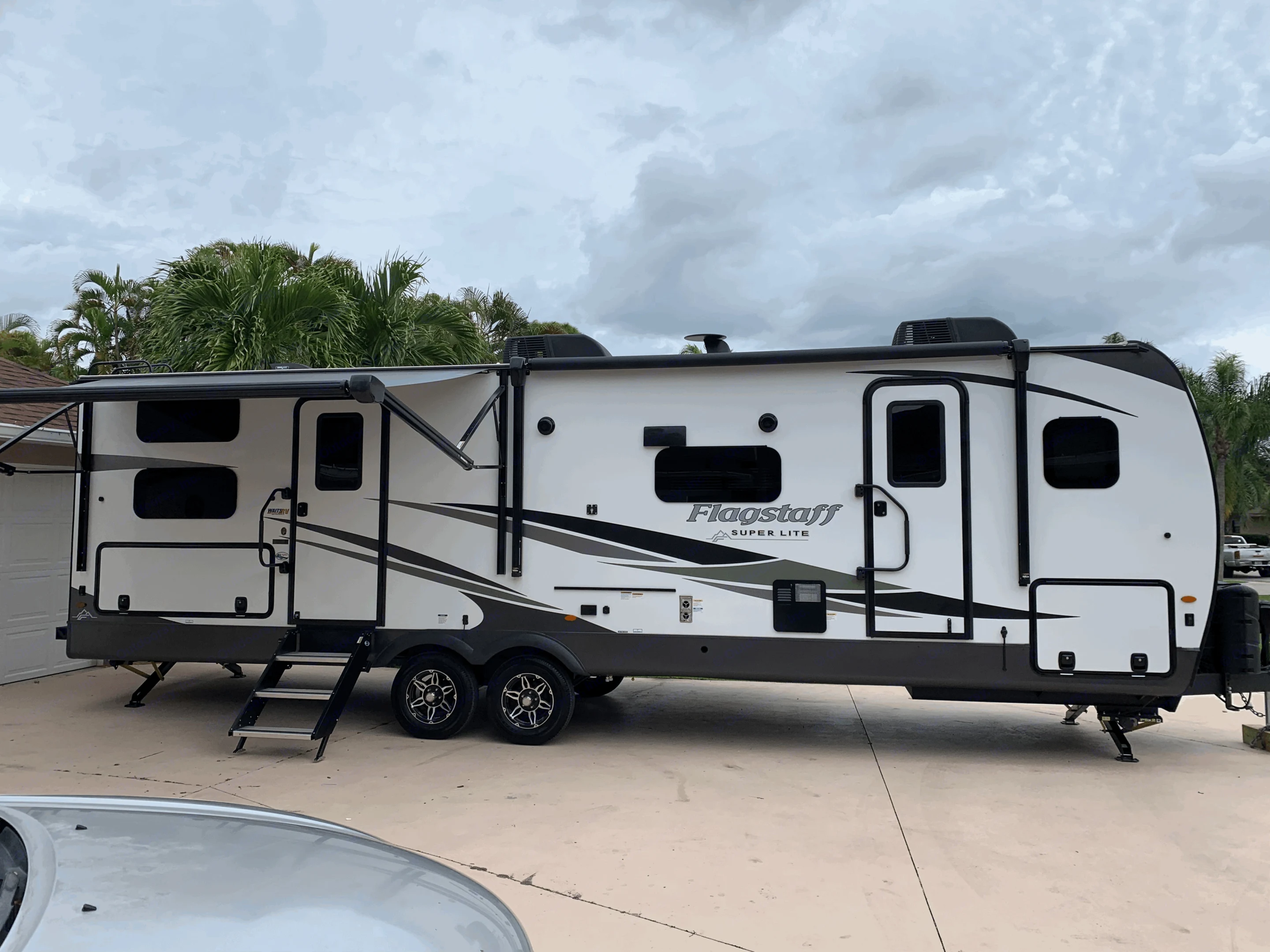A white Flagstaff Super Lite travel trailer RV rental, with black accents and an extended awning, parked on a paved driveway.. Forest River Flagstaff Super Lite 2023