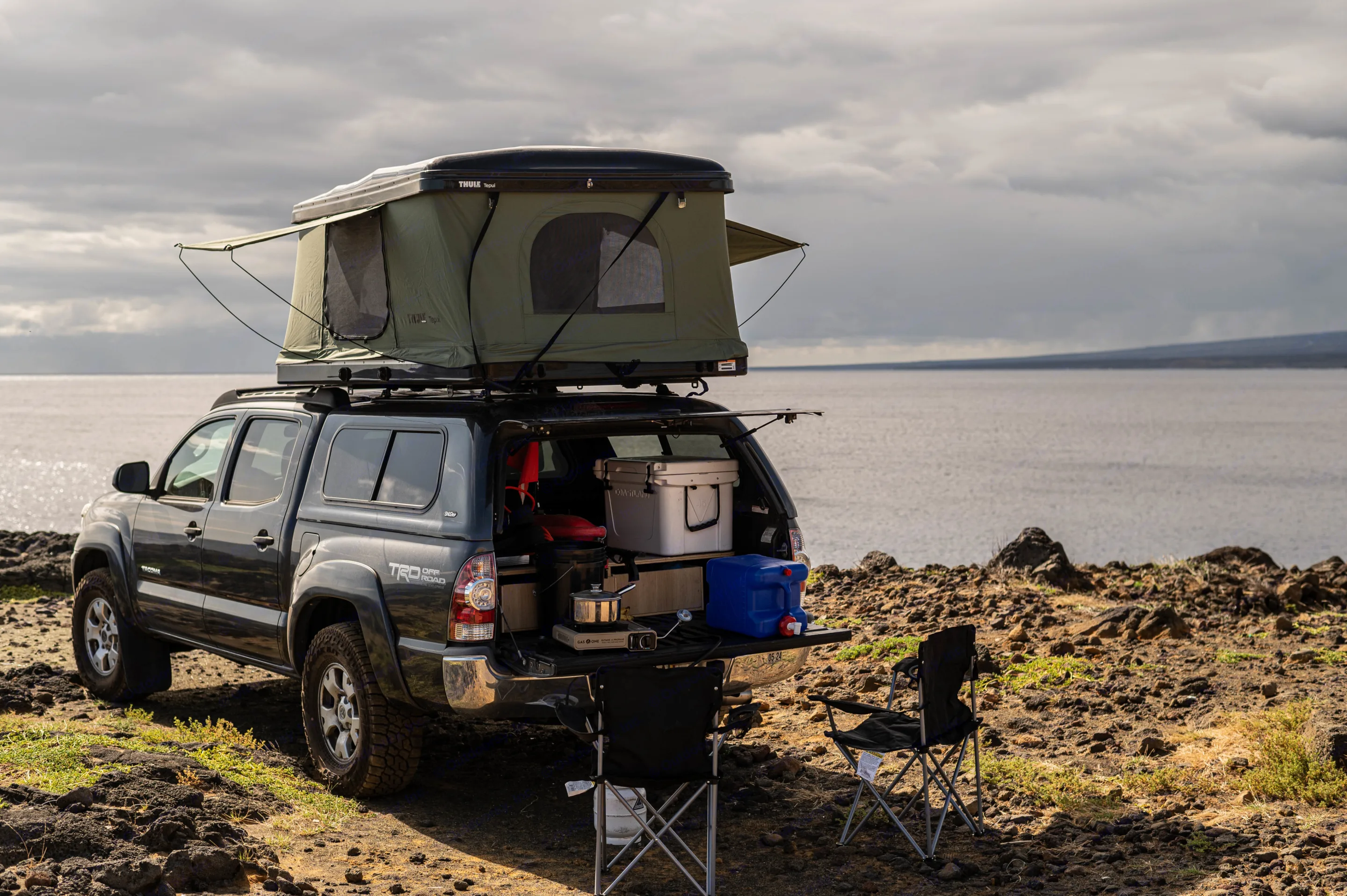 Overland RV rental: A dark pickup truck with a rooftop tent and tailgate camp kitchen by a vast body of water.. Other Other 2013