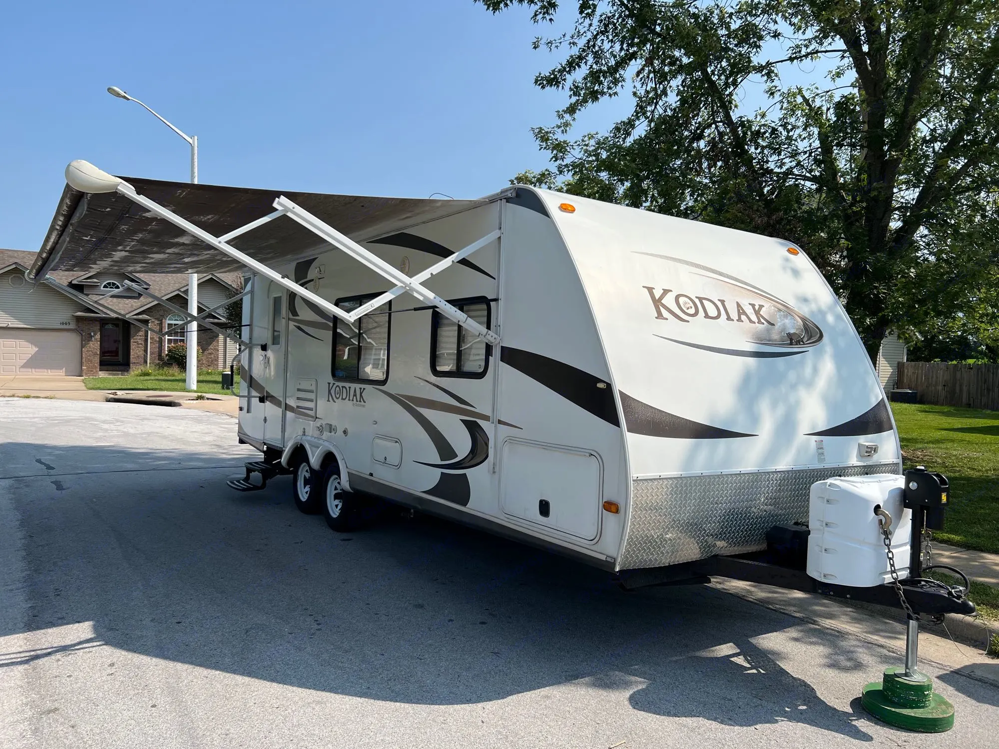 White Kodiak travel trailer with awning extended, parked on a sunny residential street.. Dutchmen Kodiak 2012
