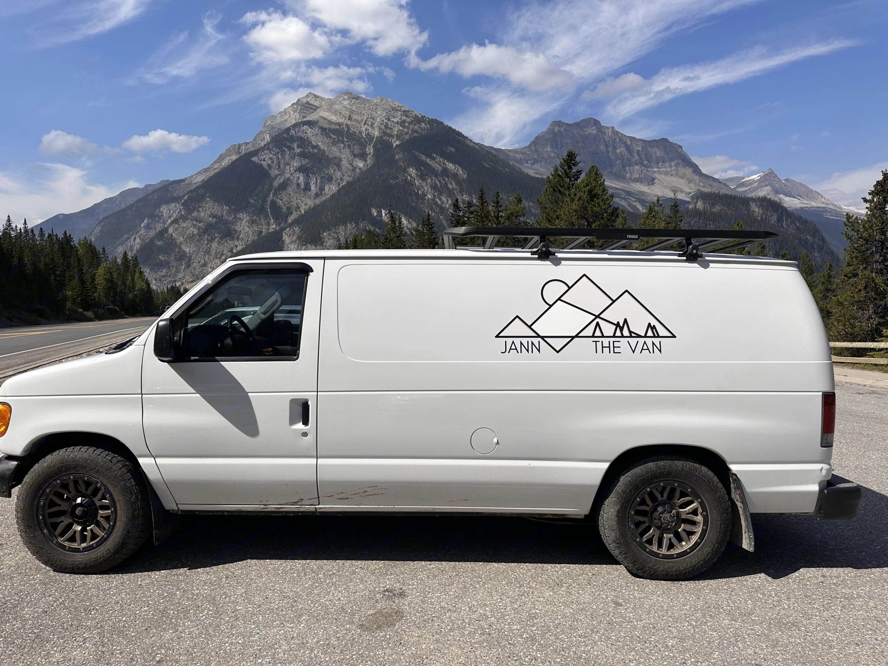 White camper van "JANN THE VAN" with roof rack, parked by majestic mountains. Your ideal RV rental for road trip adventures!. Ford Econoline 150 2005