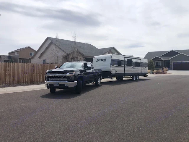 Black Chevrolet truck towing a large white Avenger travel trailer on a residential street. Explore with this RV rental setup!. Avenger ATI 2018
