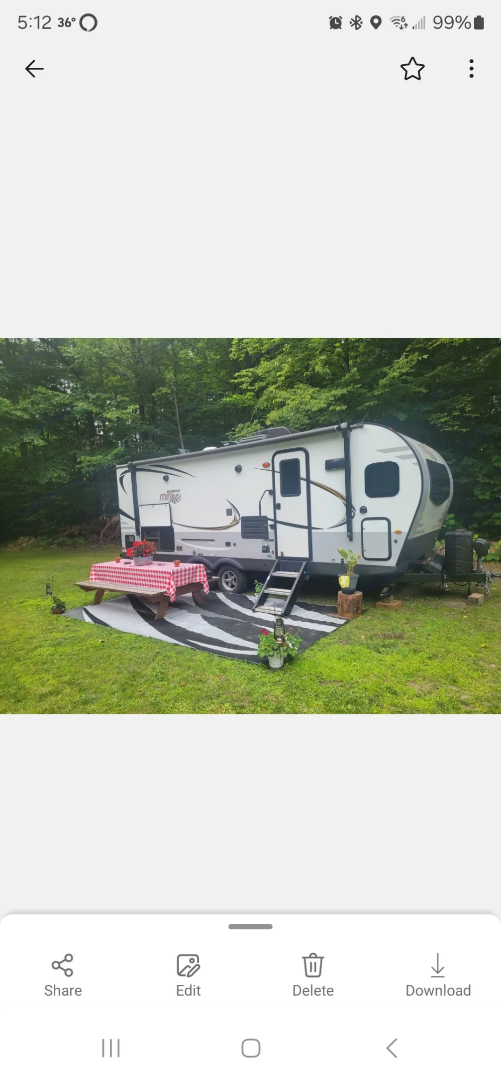 Relaxing outdoor rv rental setup with a white travel trailer, picnic table, and rug on green grass, surrounded by trees.. Forest River Rockwood Mini Lite 2021