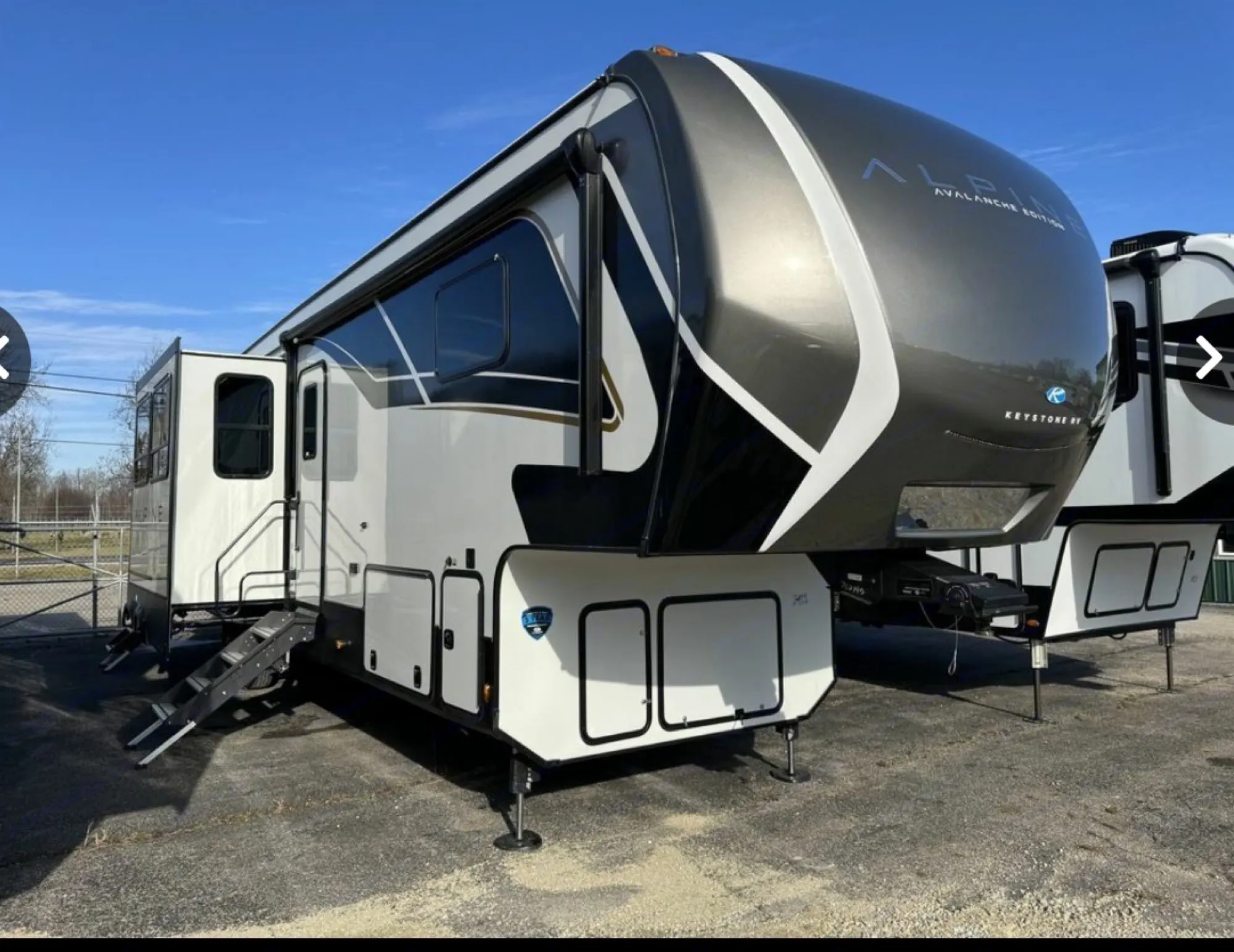 A modern, white and dark grey Keystone Alpine fifth-wheel RV rental with extended slides, parked outdoors.. Keystone Alpine Avalanche 2024