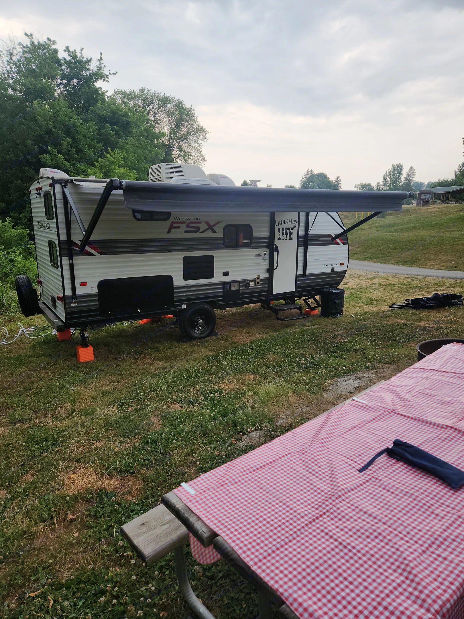 RV rental: A white Wildwood FSX travel trailer with an extended awning at a green campsite with a checkered picnic table.. Forest River Wildwood FSX 2021