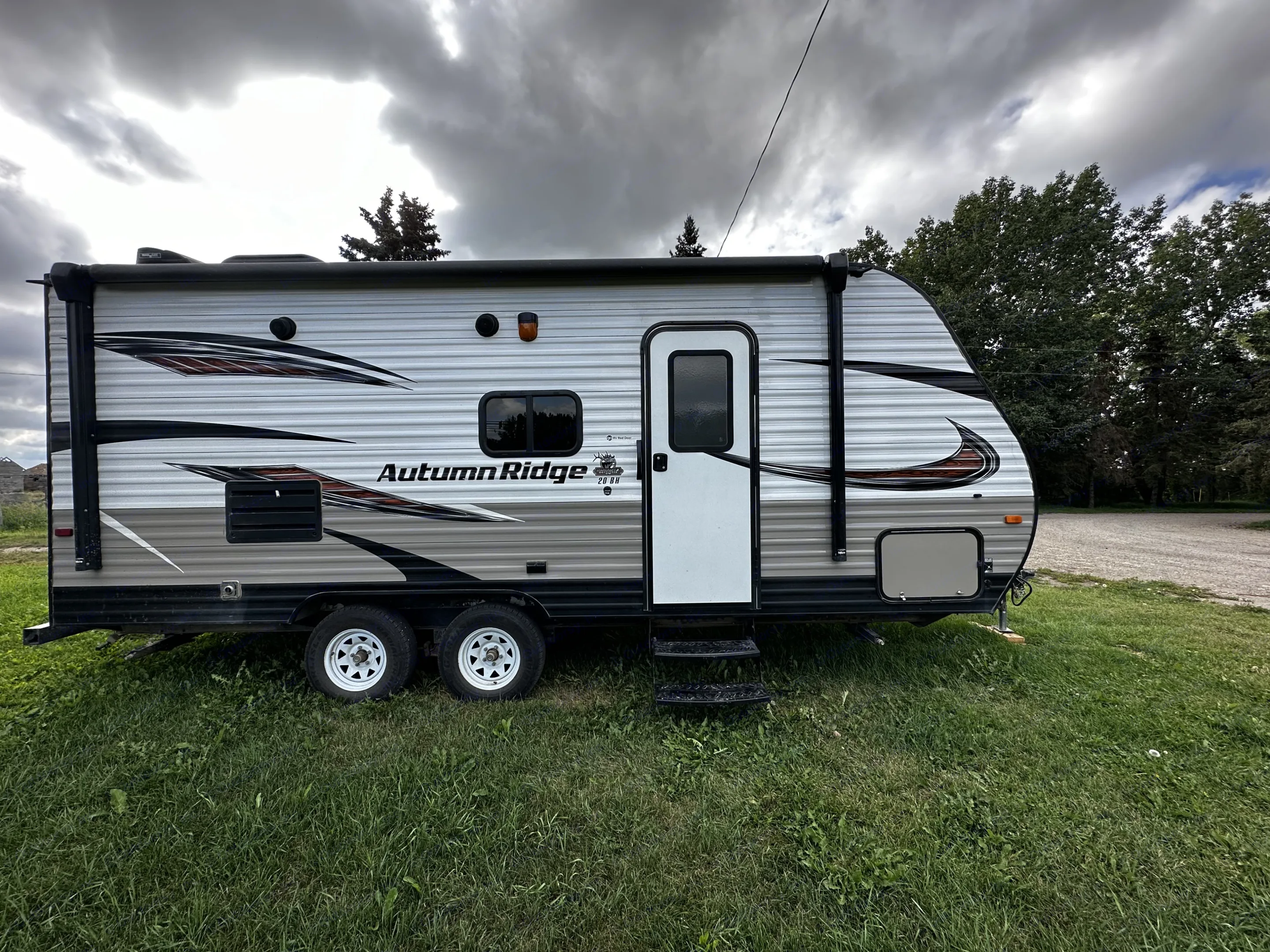 Autumn Ridge travel trailer RV rental with steps down, parked on grass under a cloudy sky.. Starcraft Autumn Ridge Outfitter 2018
