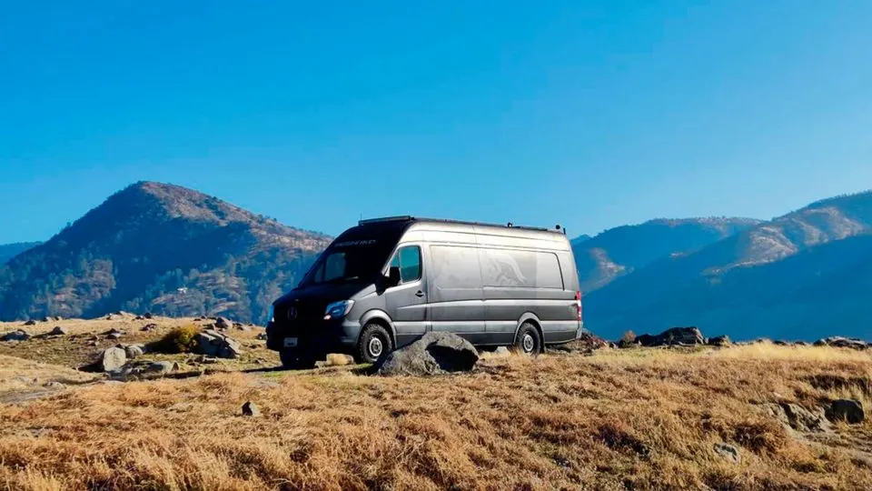 A grey Sprinter van, customized for adventure as an RV rental, sits on a grassy hill overlooking distant mountains.. Mercedes-Benz Sprinter 2015