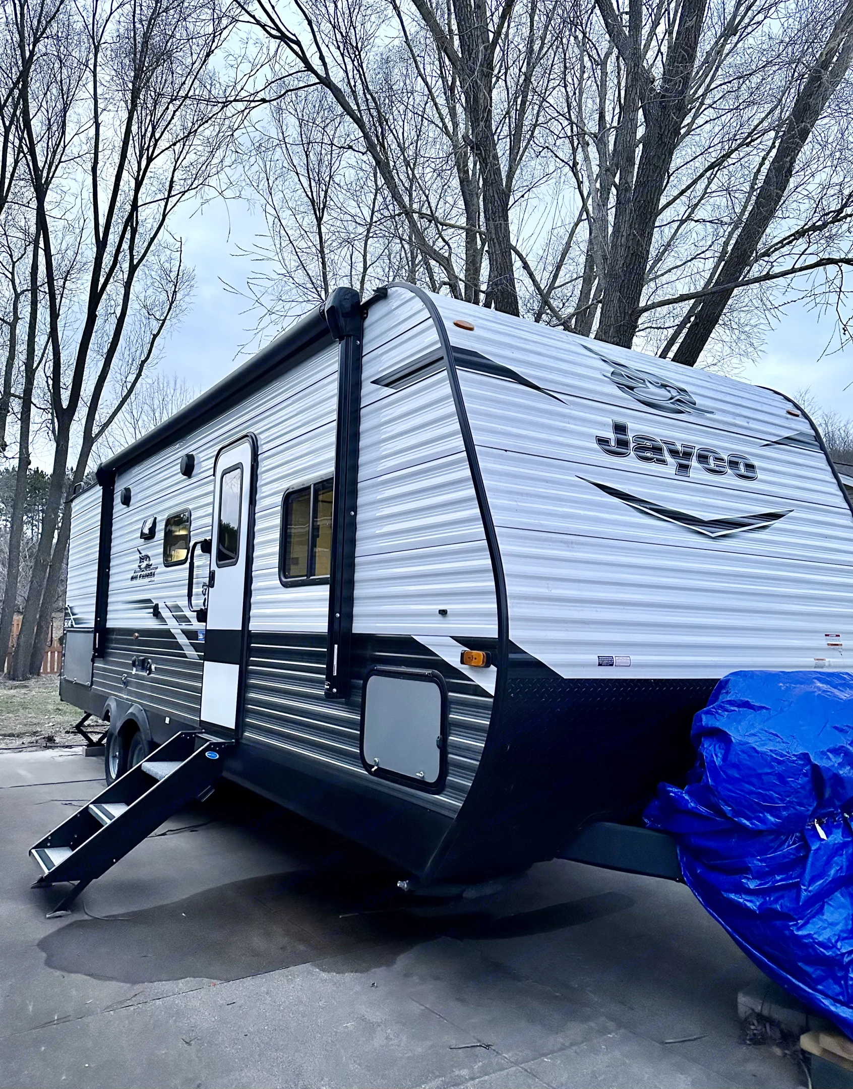Jayco travel trailer RV rental, parked on asphalt with steps down. Bare trees against a cloudy sky complete the scene.. Jayco Jay Flight SLX 2022