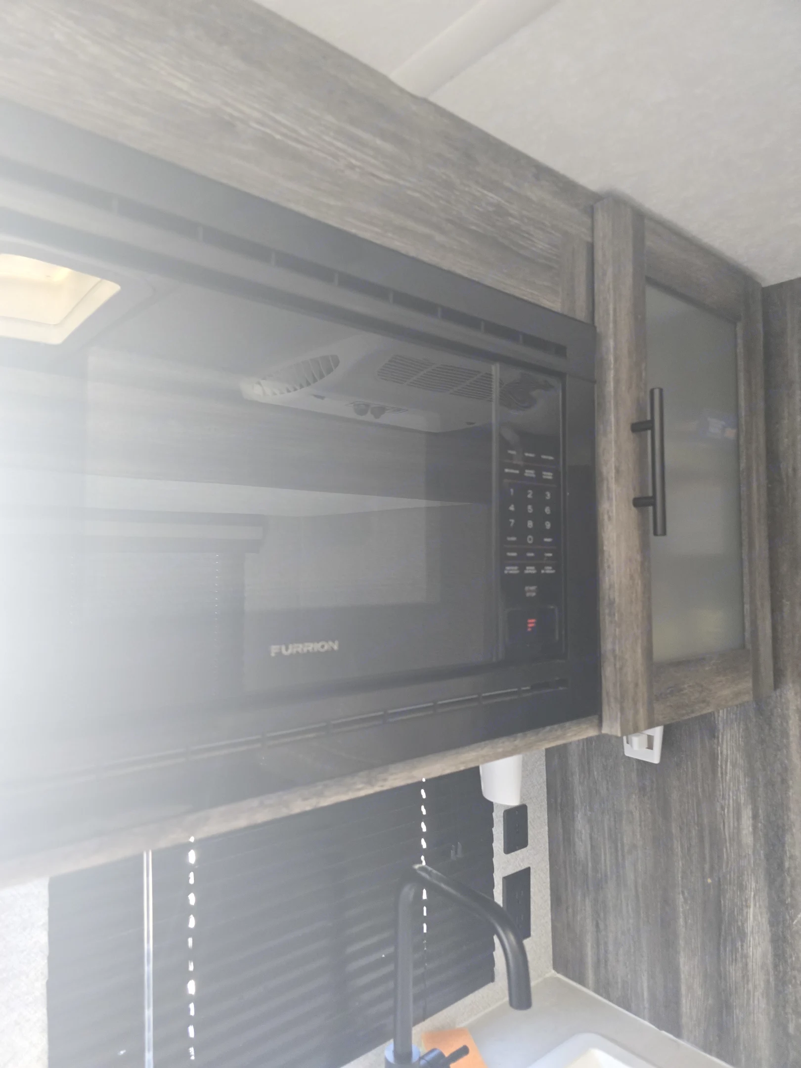 Modern RV rental kitchen with an overhead Furrion microwave, sink, and wood-grain cabinets for comfortable travel.. Forest River Wildwood FSX 2021