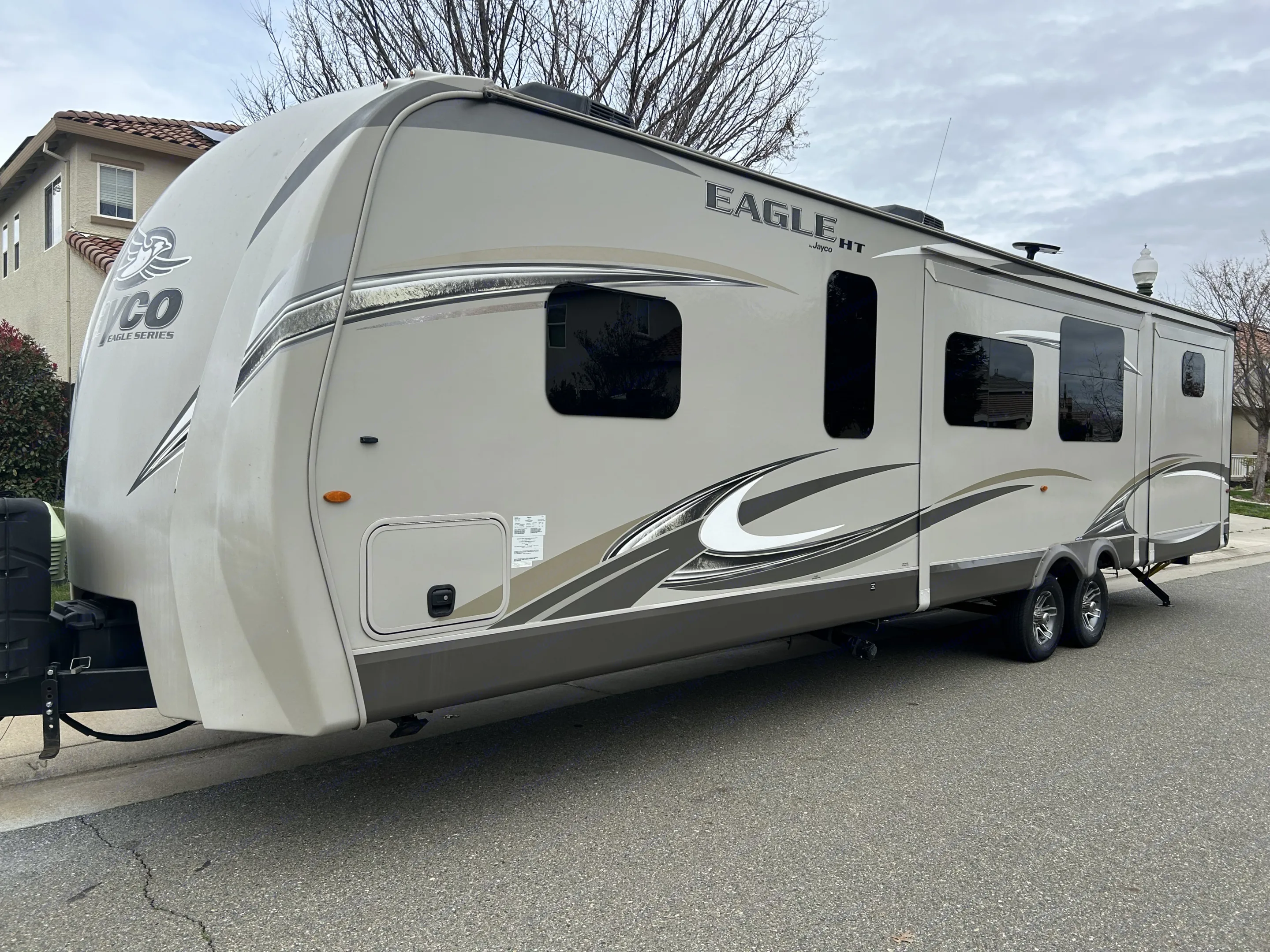A large, light-colored Jayco Eagle HT travel trailer, often used as an RV rental, is parked on a residential street.. Jayco Eagle HT 2018