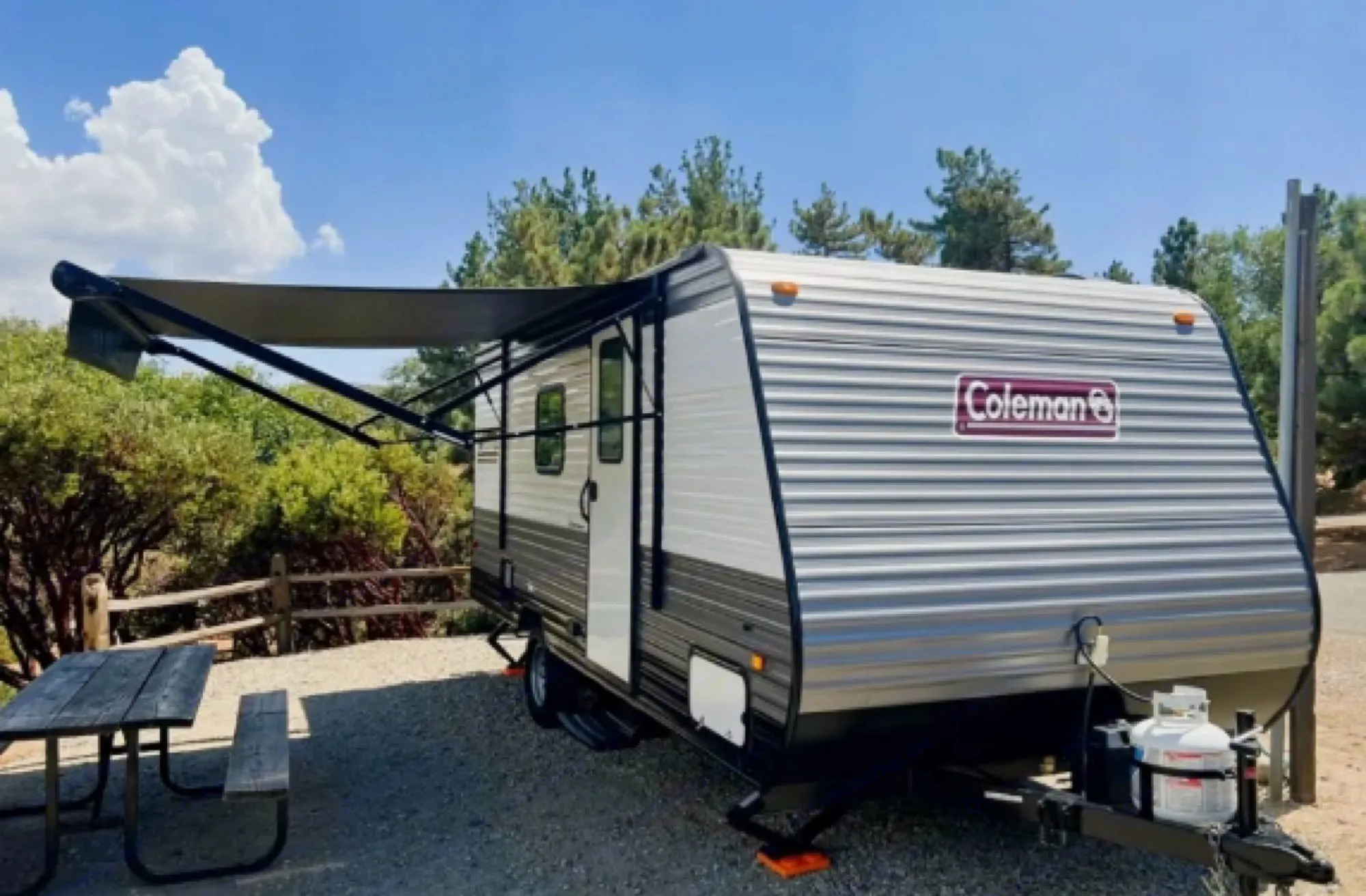 This RV rental features a travel trailer parked on a gravel campsite, with an extended awning and a picnic table nearby.. Coleman Lantern 17b 2024
