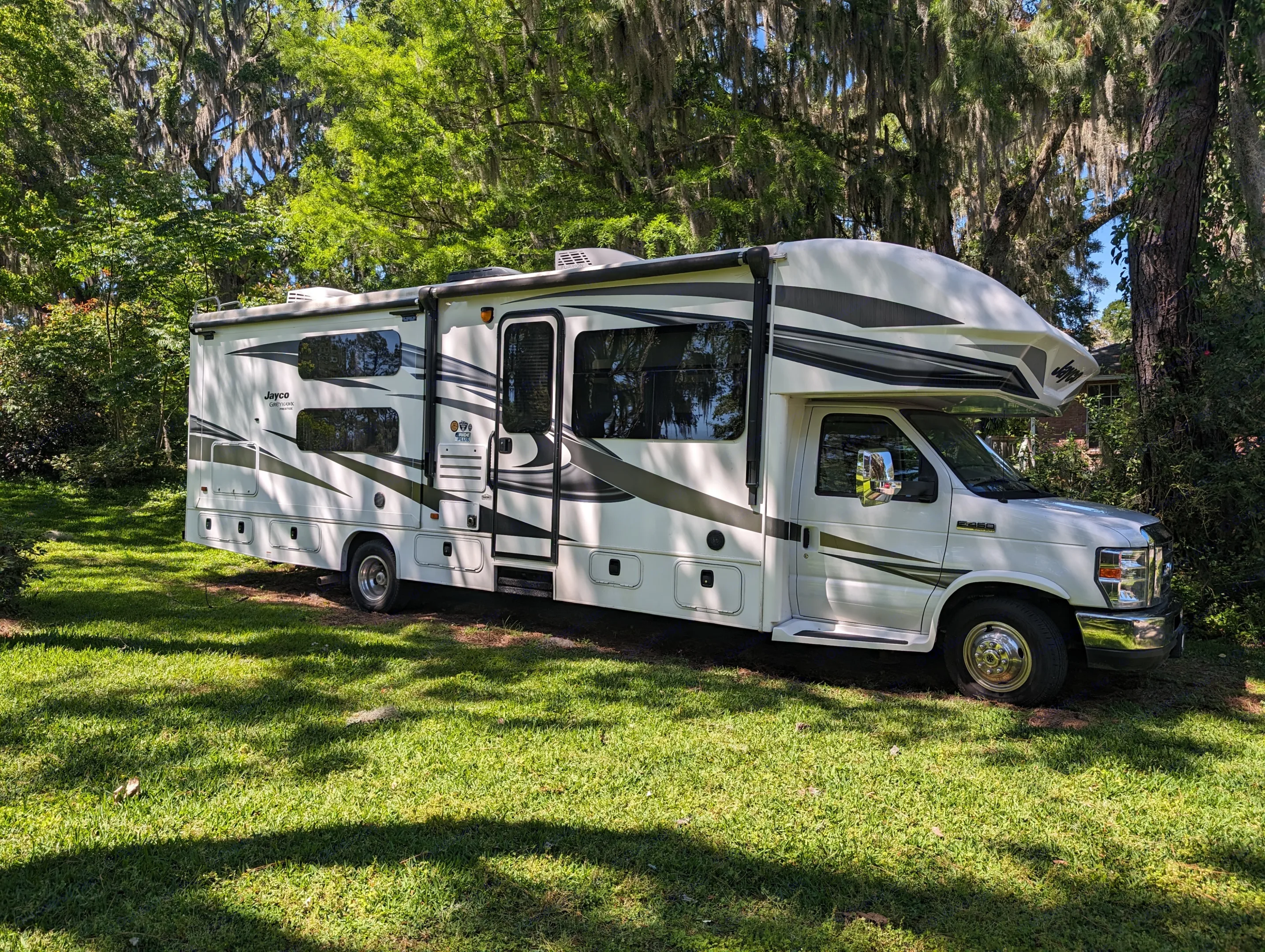 White Jayco RV rental parked on green grass under shady trees, ideal for road trips and camping adventures.. Jayco Greyhawk 2019