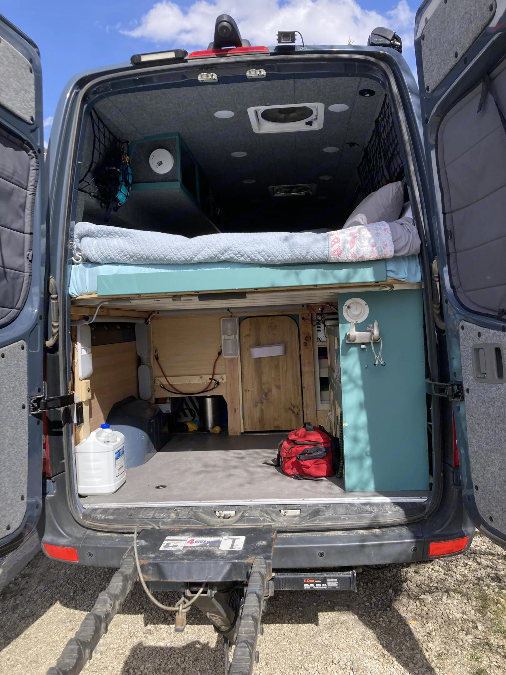 Open rear doors of an RV rental, revealing a well-designed van conversion with a bed, storage, and essential utilities.. Mercedes Sprinter 2018