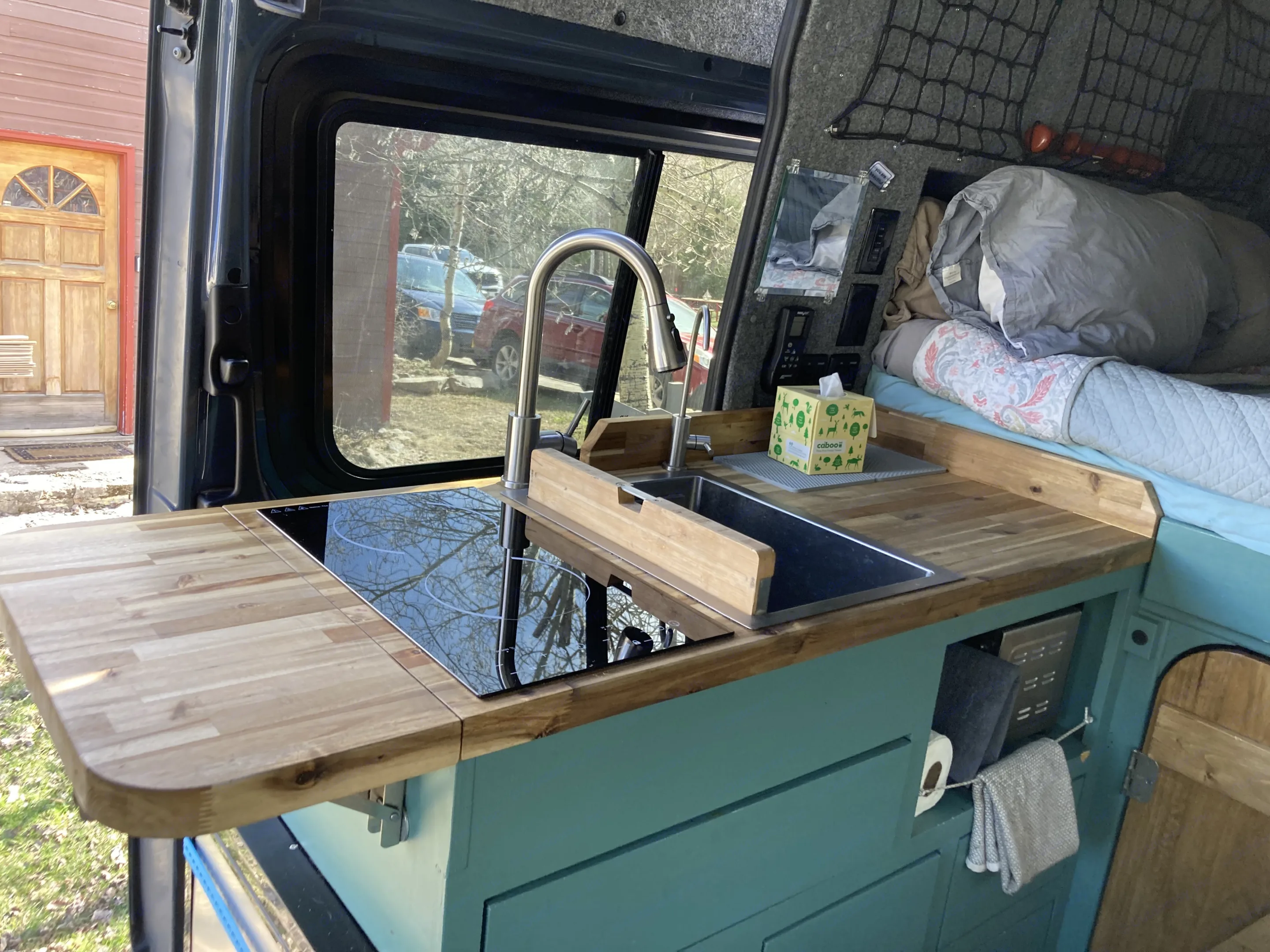 Compact RV rental kitchen with sink, cooktop, and bed, offering mobile comfort for travel.. Mercedes Sprinter 2018