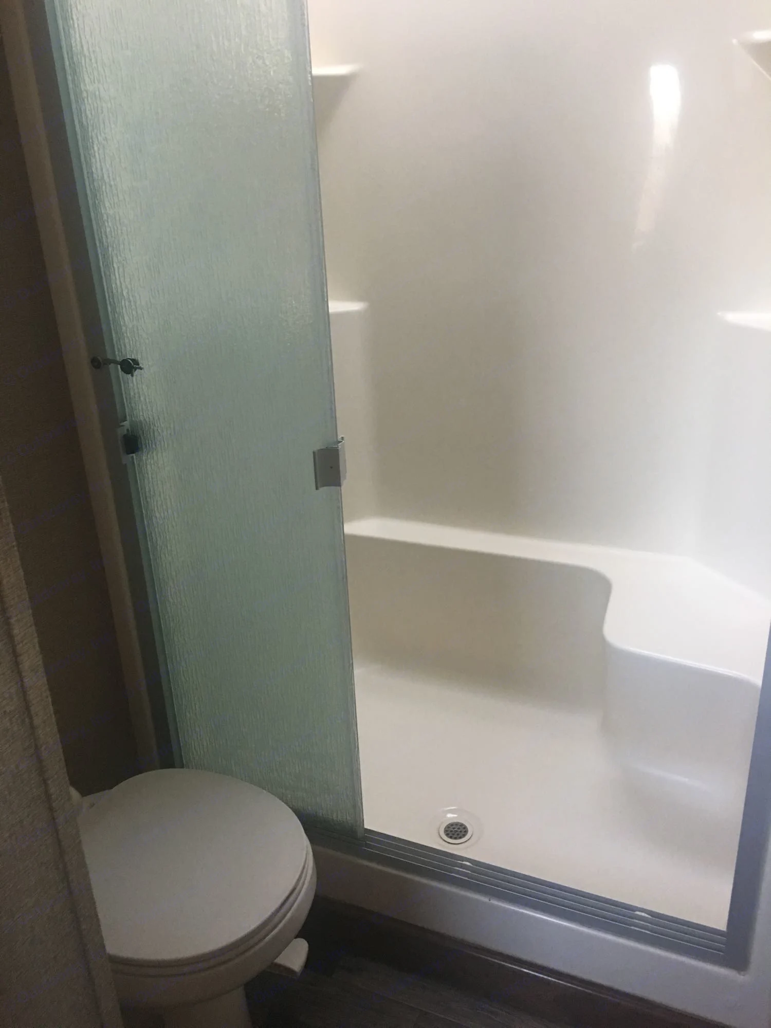 Compact RV rental bathroom features a frosted glass shower with a built-in bench and a toilet.. Keystone Montana 2015
