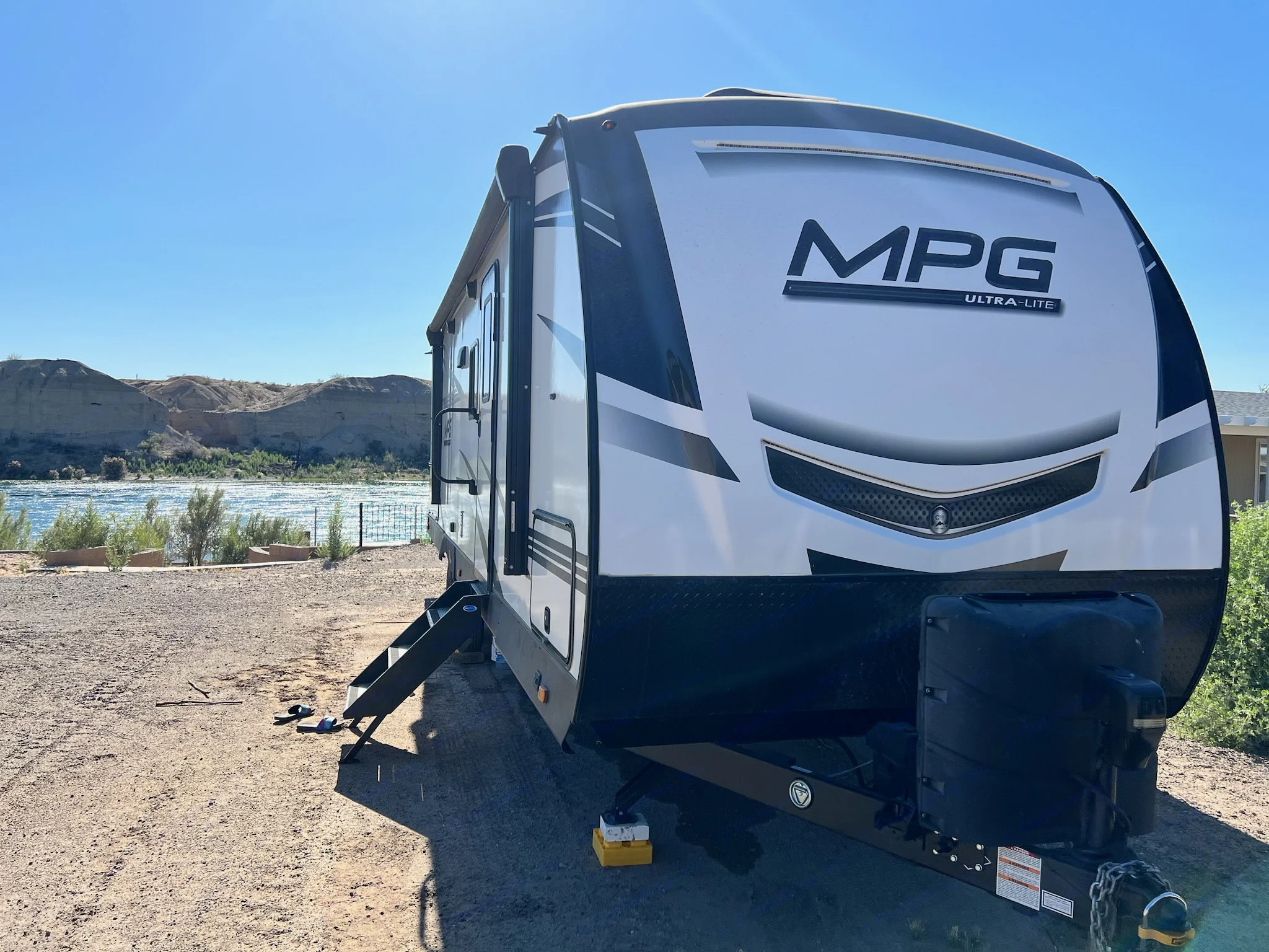 Scenic rv rental view: A white travel trailer by a river and hills under a clear blue sky, ideal for outdoor travel.. Cruiser RV MPG Ultra Lite 2021