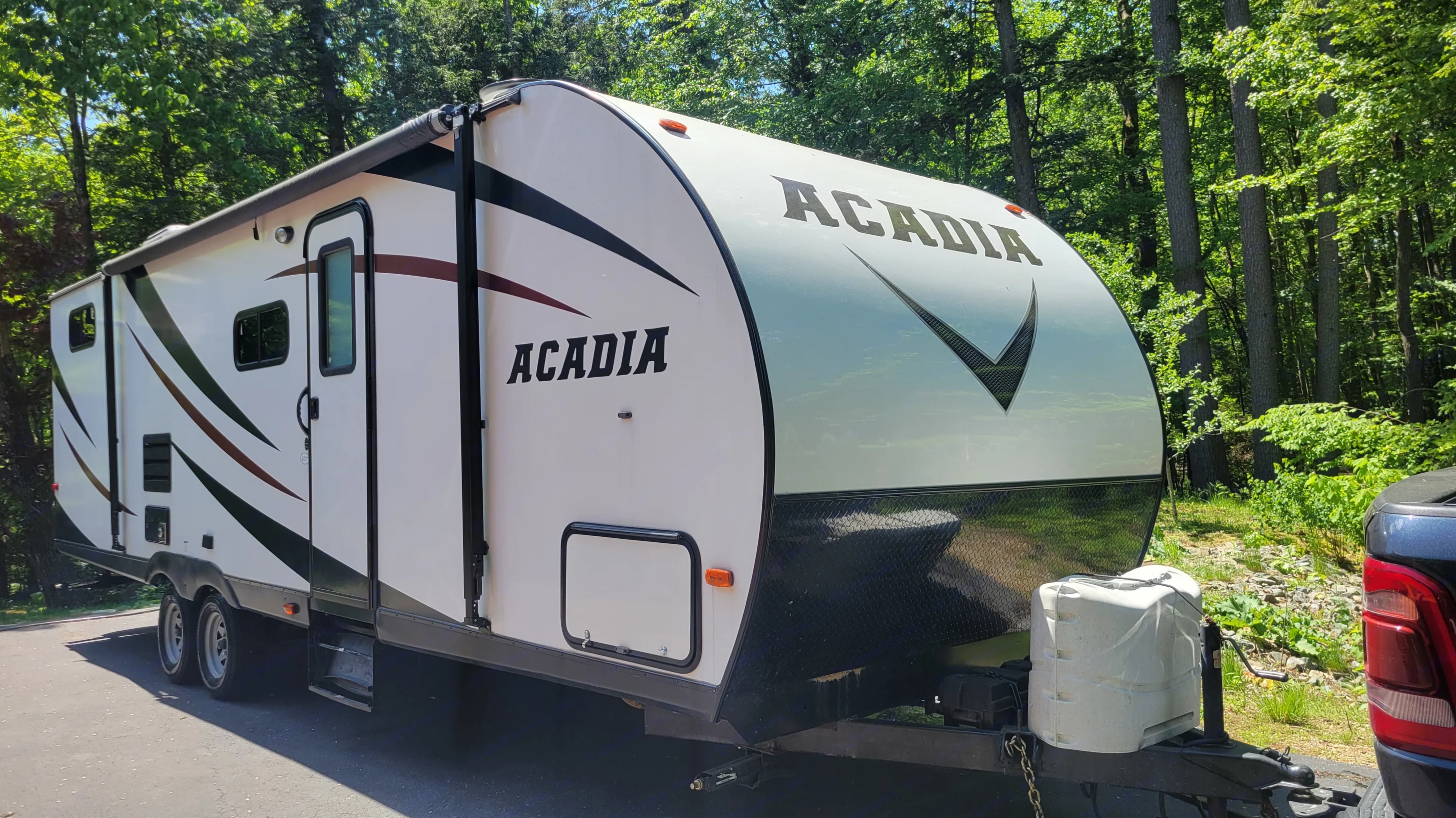 A white Acadia RV rental travel trailer with black accents is parked among green trees, perfect for camping adventures.. Forest River Acadia 2018