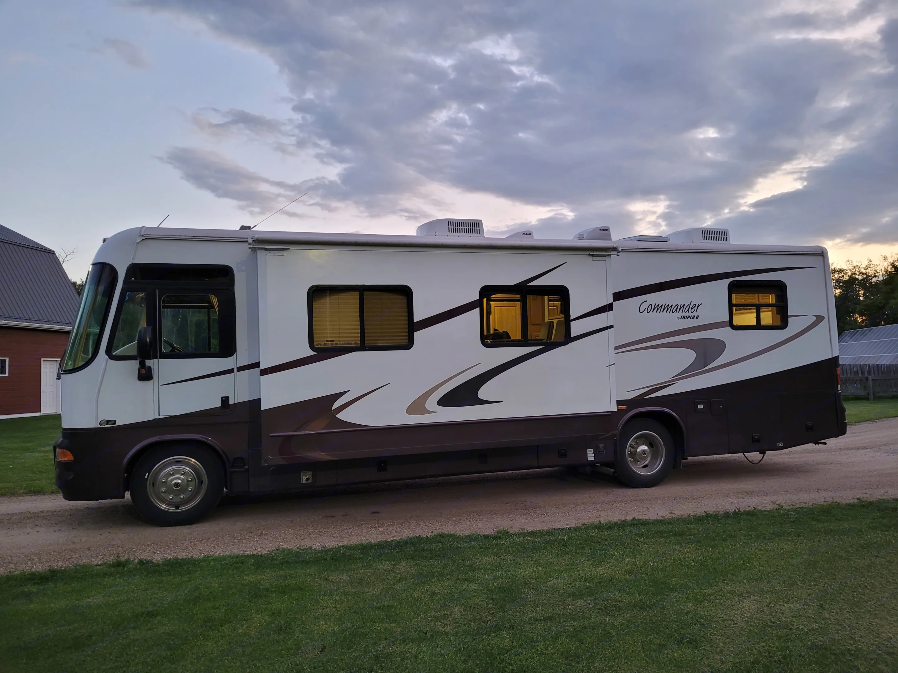 Experience travel in this spacious Commander motorhome, a white and brown RV rental. Parked at dusk with lights on.. Triple E Commander 2004