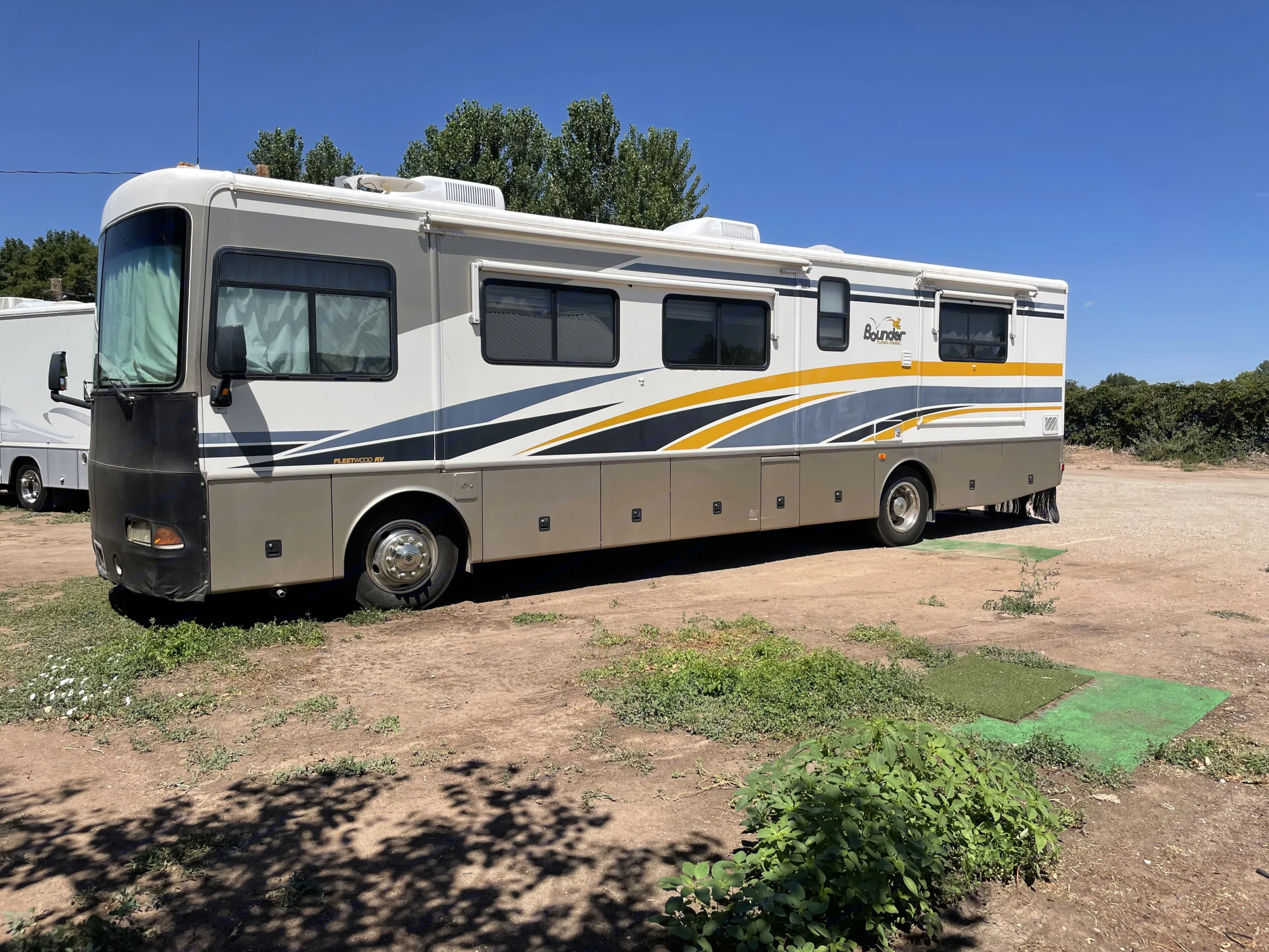 Fleetwood Bounder RV rental parked on a dirt lot with green turf. A spacious motorhome under a clear blue sky.. Fleetwood Bounder 37U 2003