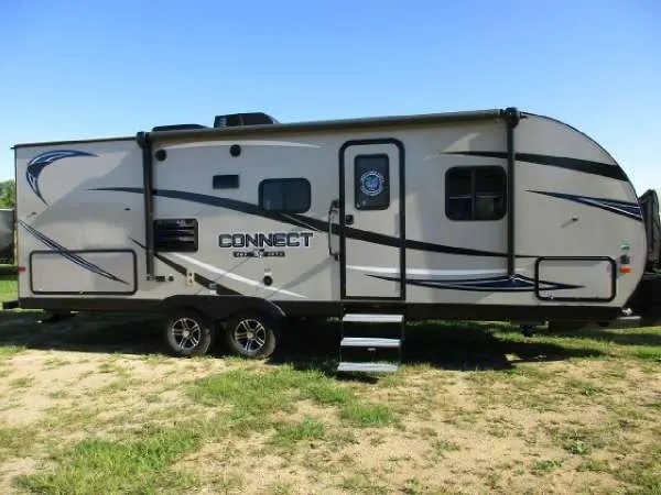 Light gray travel trailer (RV) with "CONNECT" logo, available for rv rental. Parked on grass. KZ Connect 214bhk 2018