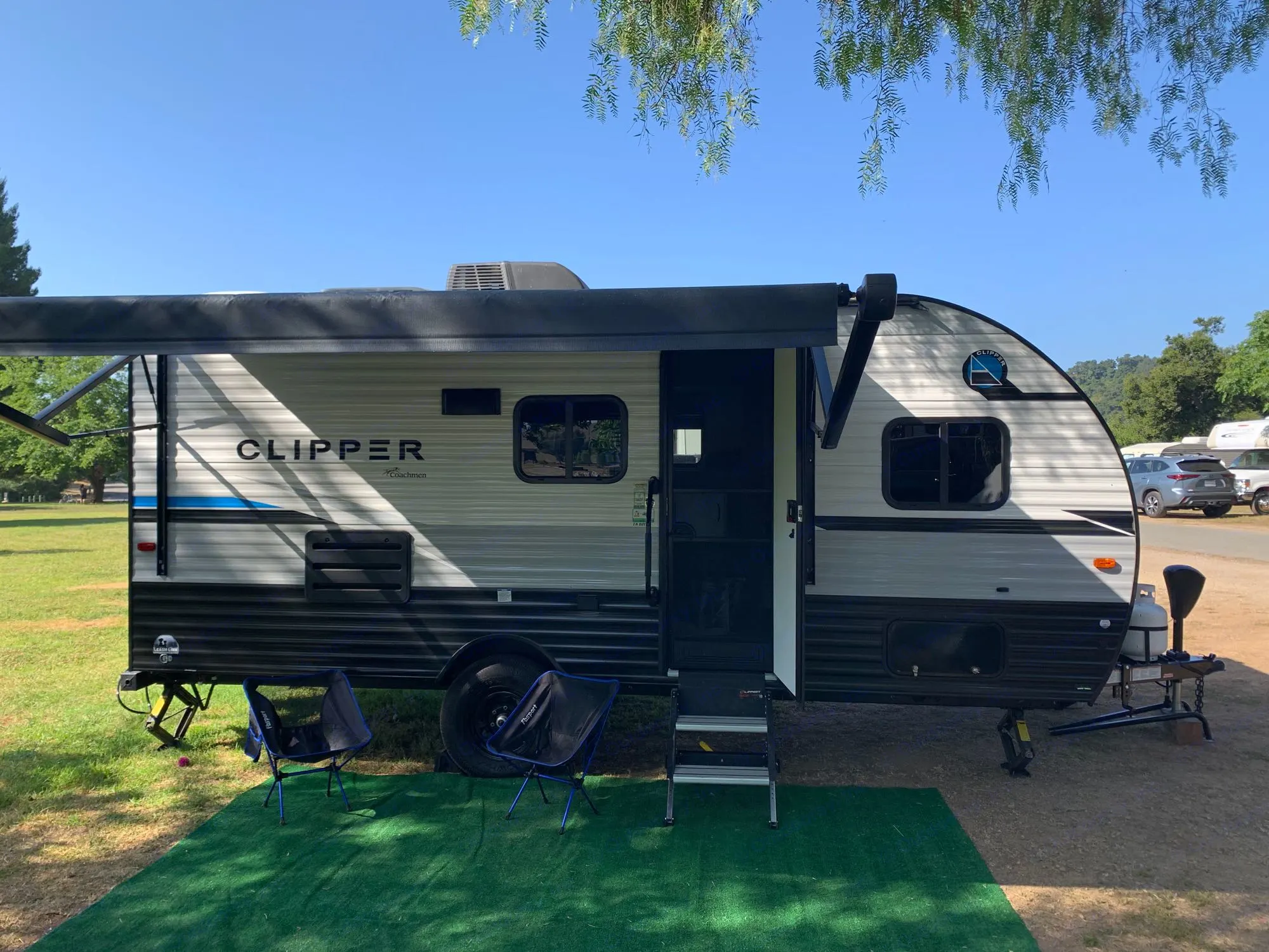 This Clipper travel trailer RV rental is set up for a sunny day of camping, featuring an awning, steps, and comfy chairs.. Clipper 18BHS 2023