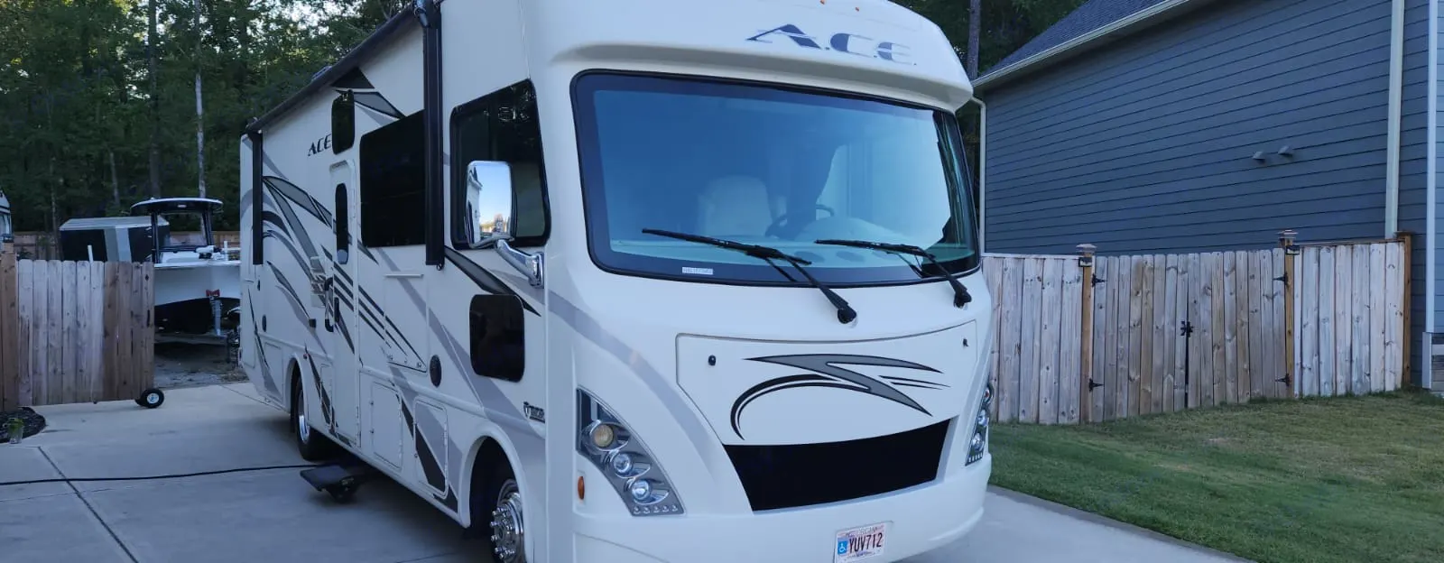 Large cream ACE motorhome RV rental parked on a driveway, with a boat & fenced yard visible in the background.. Thor A.C.E. 2018