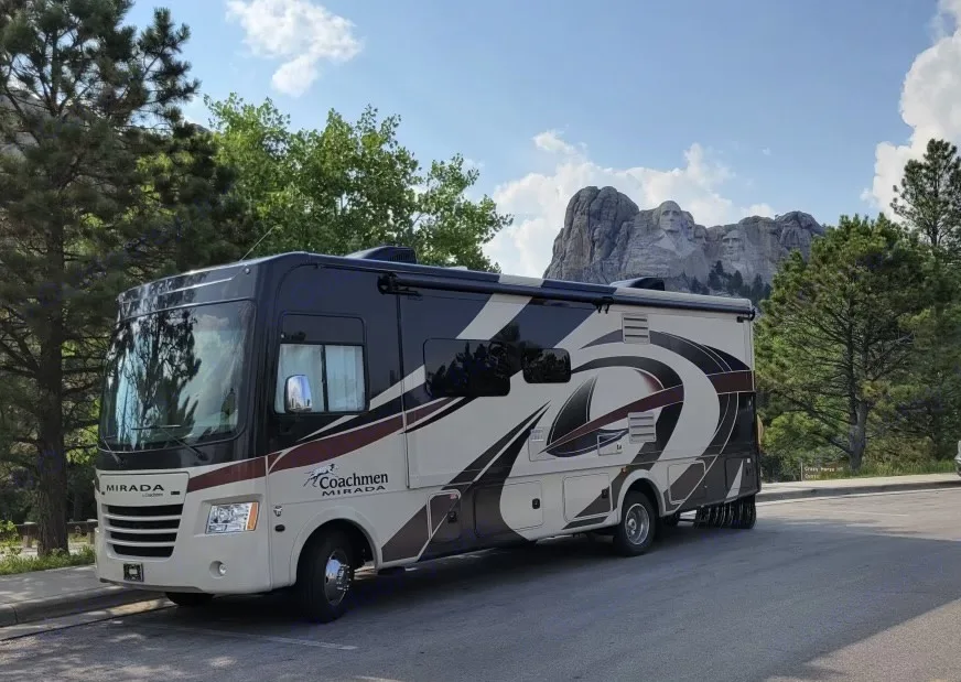 An rv rental is parked in front of Mount Rushmore, showcasing the iconic presidential sculptures carved into the mountain. Coachman Mirada 2018