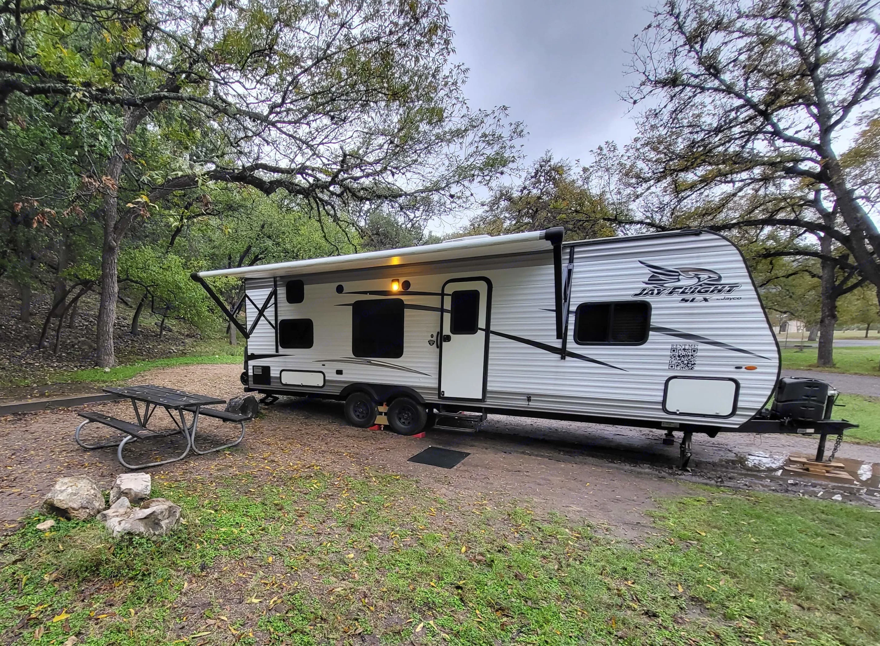This Jayco RV rental is set up at a rustic campsite with a picnic table, ready for your adventure under the trees.. Jayco Jay Flight SLX 2017
