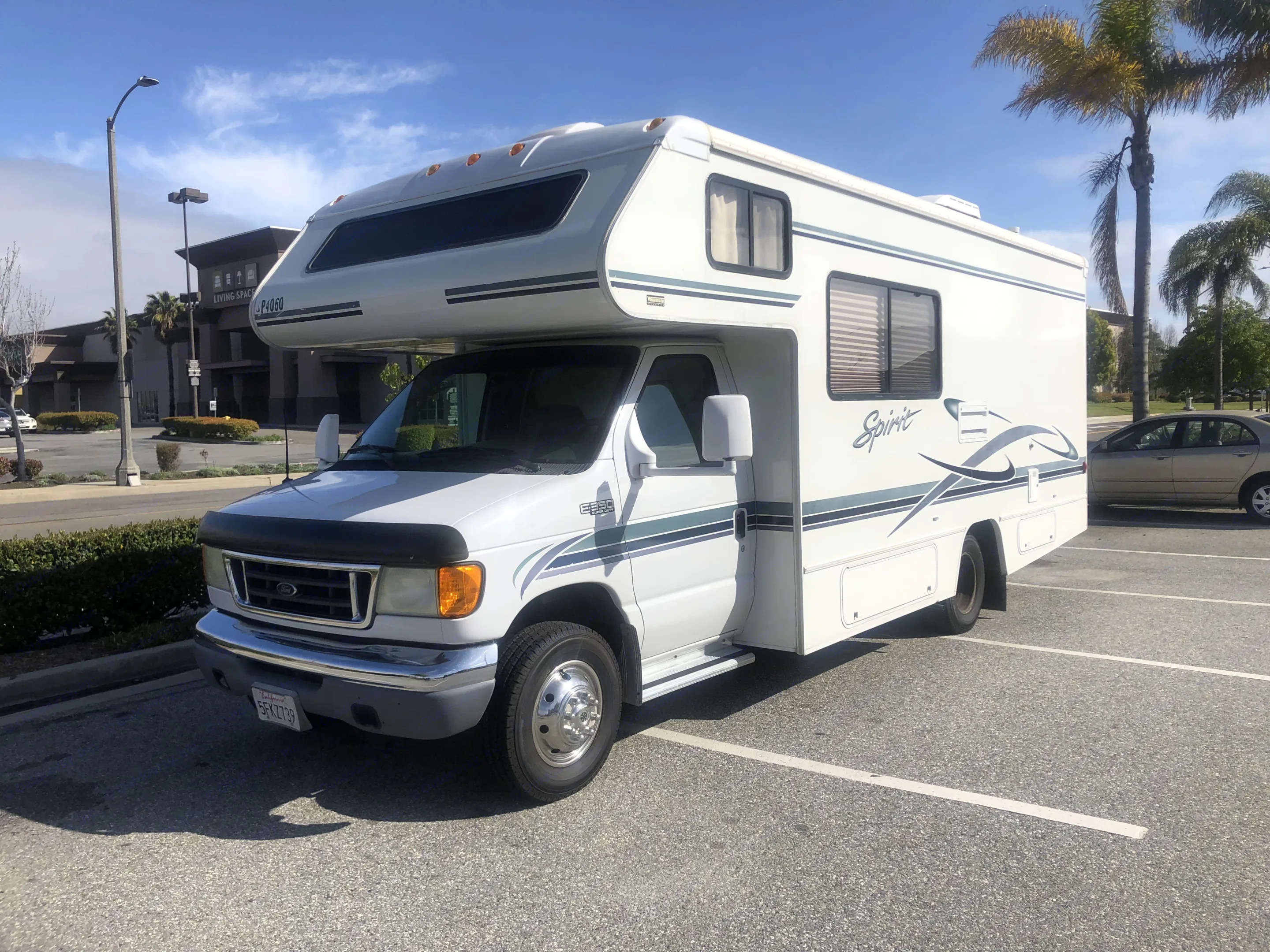 This white Class C RV rental, a Ford E-350 Spirit, is parked in a sunny outdoor lot.. Itasca Spirit 2004