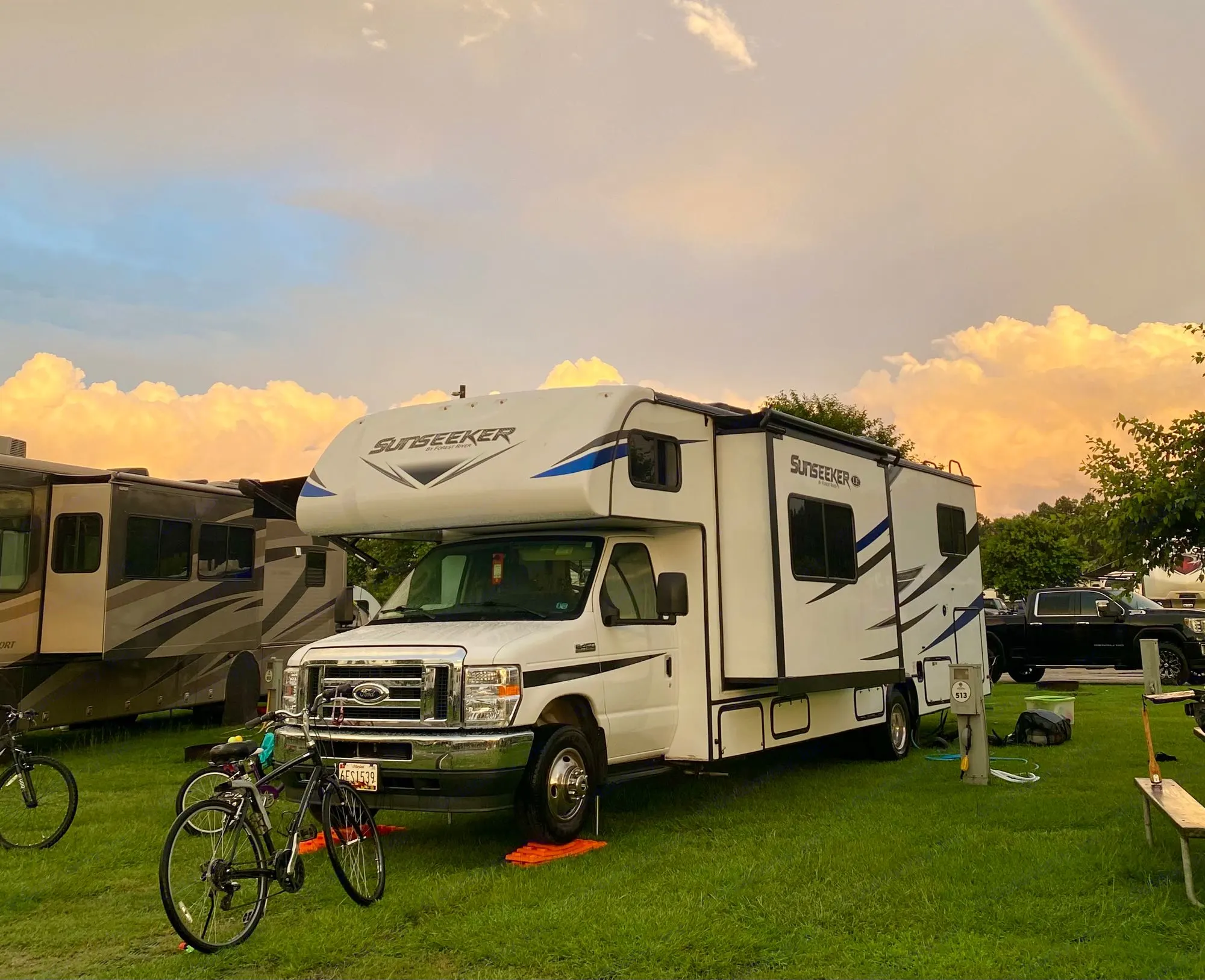 A spacious white rv rental parked at a green campsite, bathed in the warm glow of a sunset sky. Perfect for family trips.. Forest River Sunseeker 3250DSLE 2022