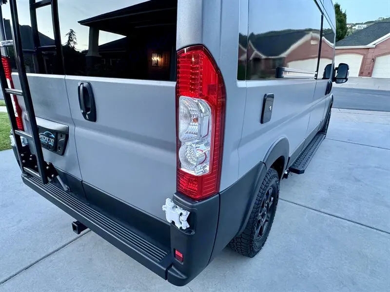 This gray RV rental, a custom camper van, features a rear ladder, side steps, and rugged tires for adventure.. Dodge Ram 1500 2021