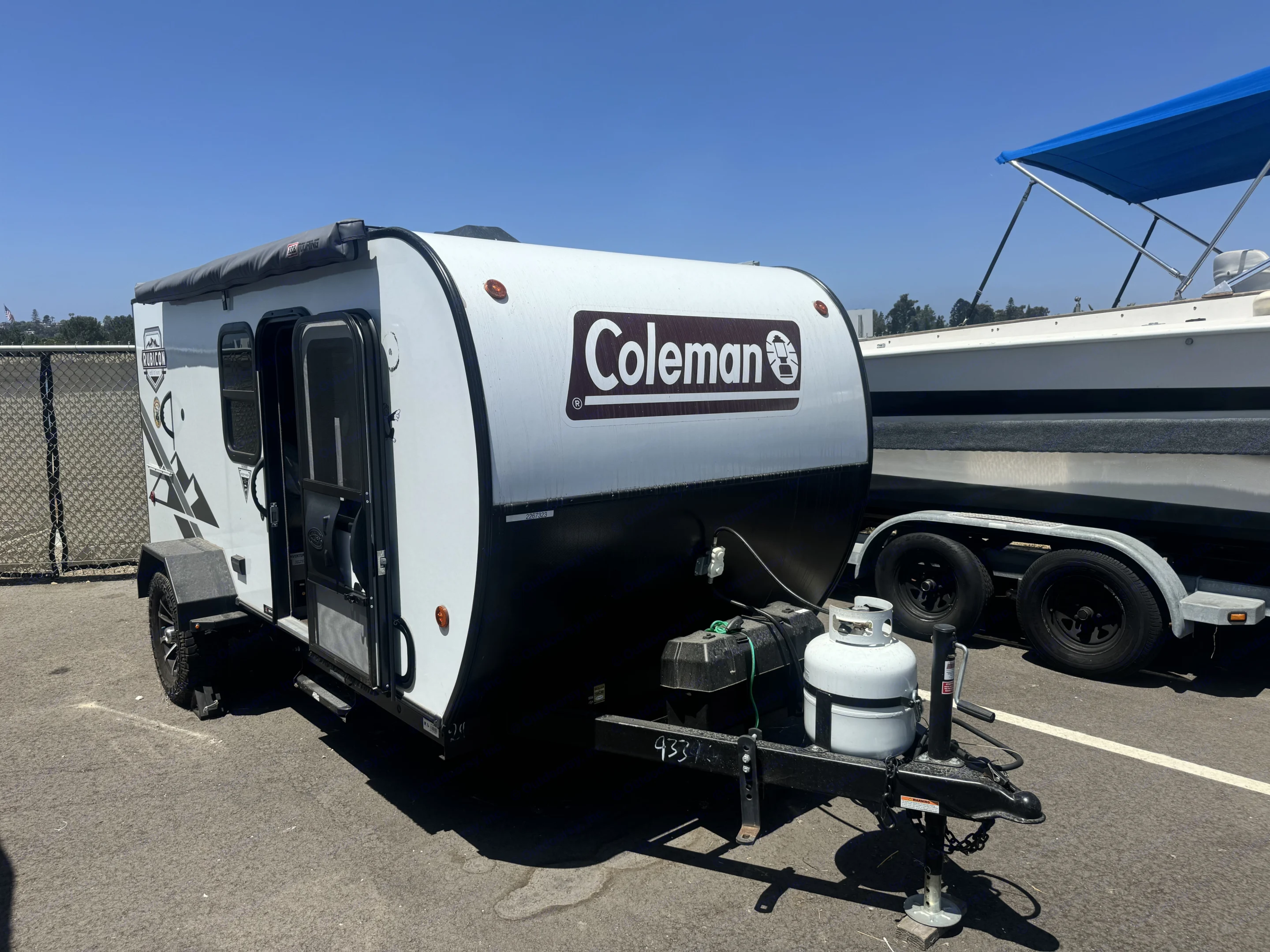A white and black Coleman camper trailer (RV rental) is shown on asphalt, parked beside a boat. Ready for outdoor adventures.. Rubicon 4YDTCHME10RJ933964 2024