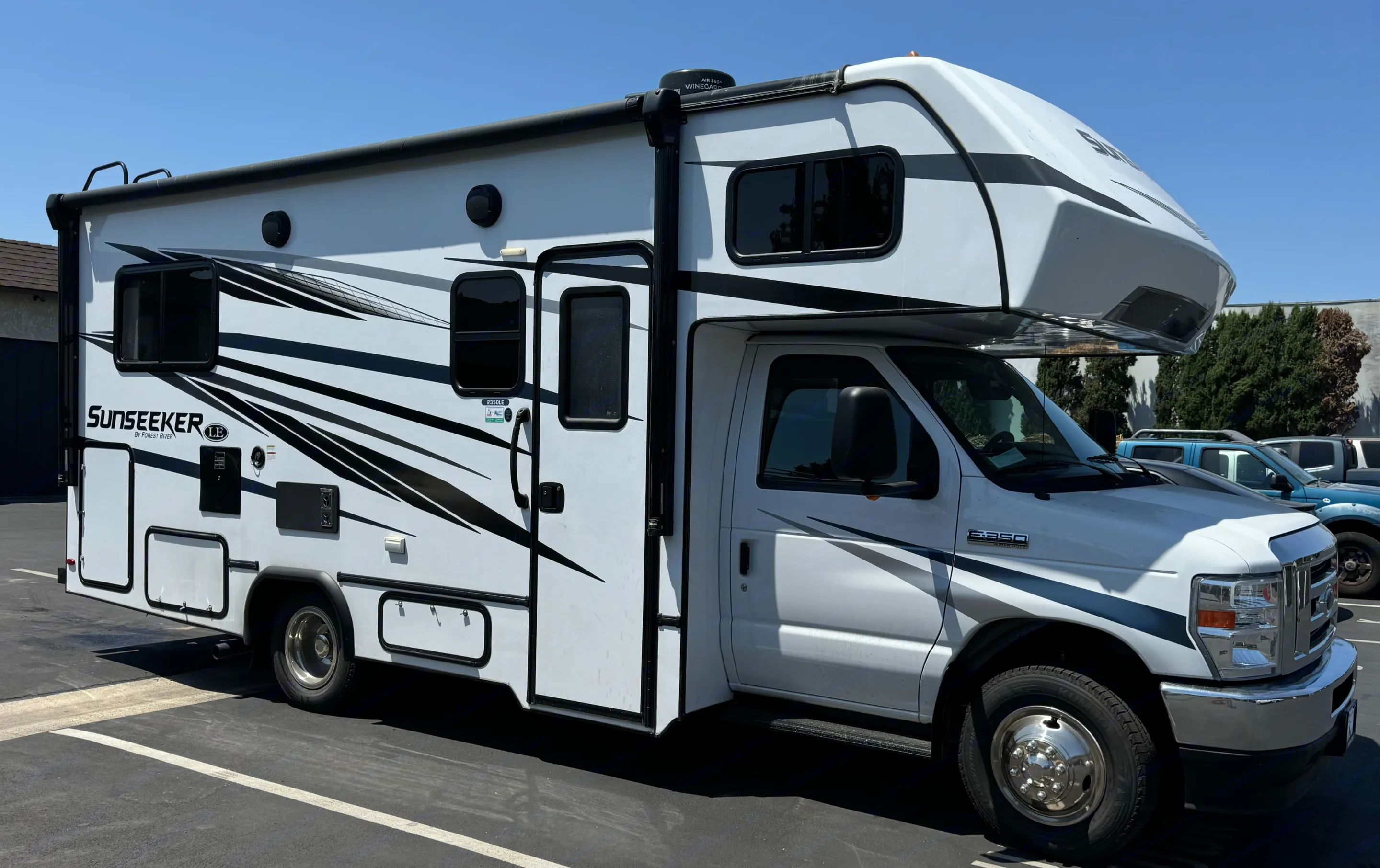 A white Forest River Sunseeker 2350LE rv rental, parked on asphalt under a clear blue sky.. Forest River Sunseeker LE 2023