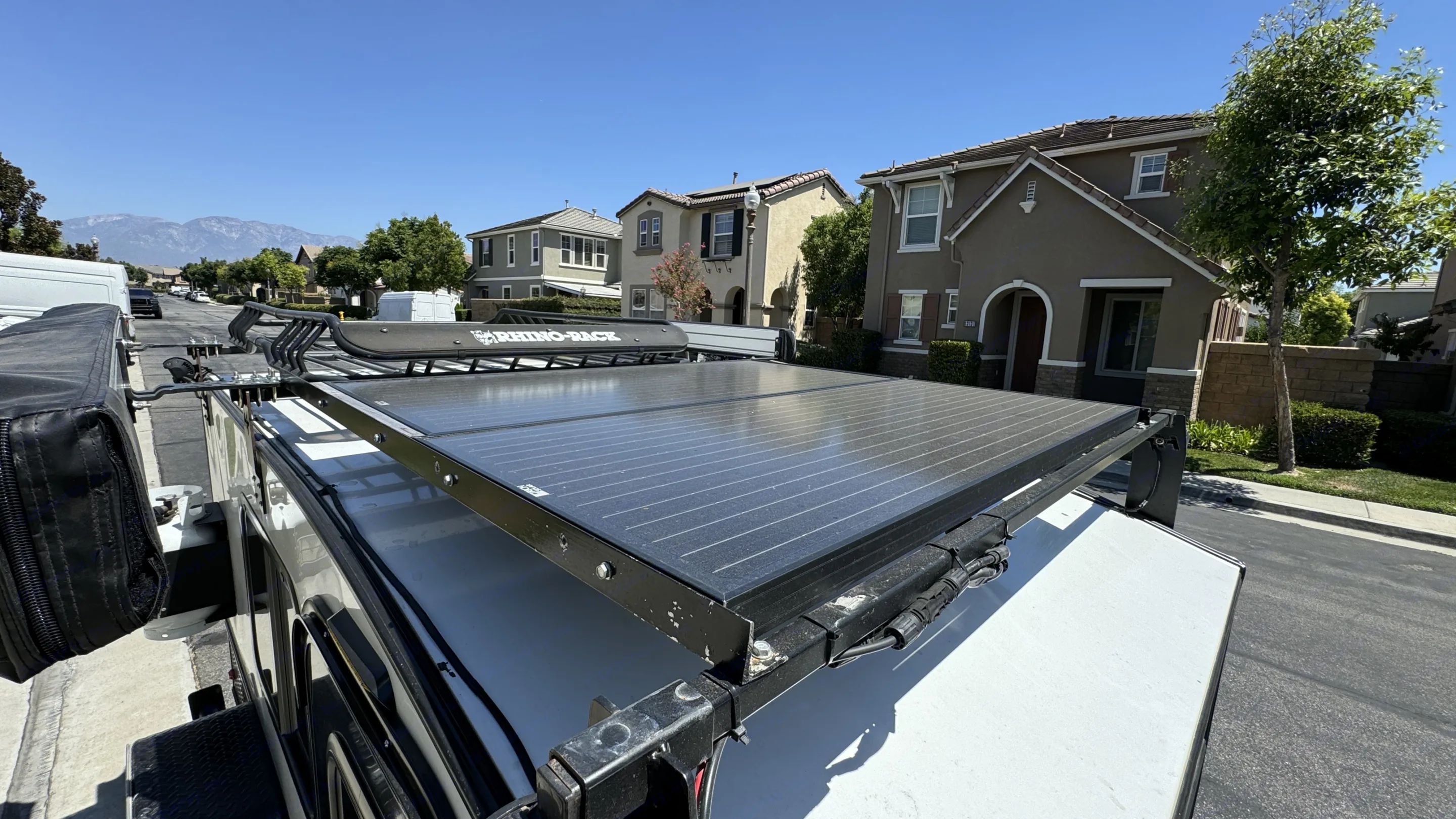 Solar-equipped RV rental featuring a Rhino-Rack system with rooftop panels. Parked on a sunny street with distant mountains.. Hiker Trailer Mid-Range Off Road 2019