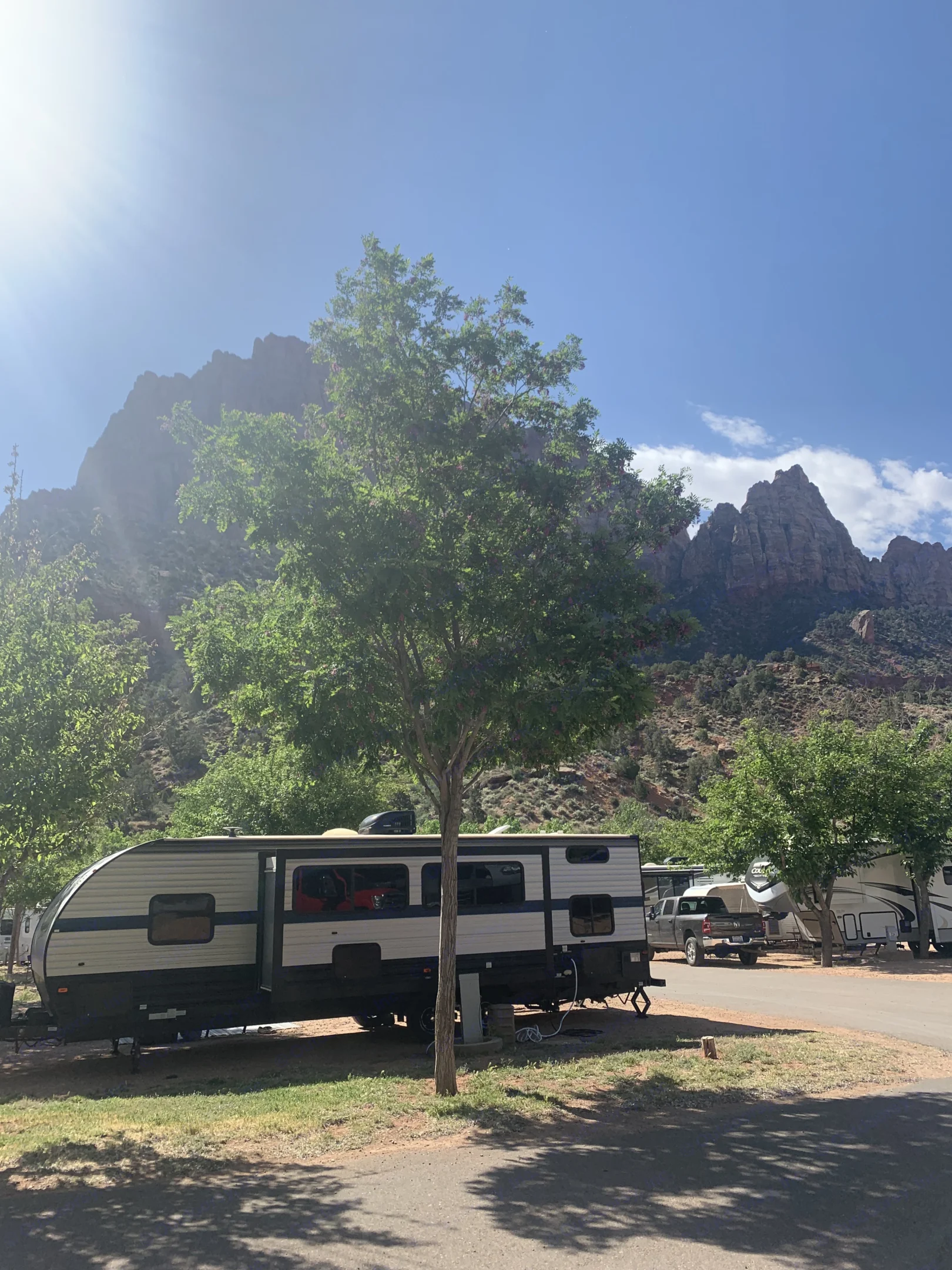 Scenic RV rental campsite nestled among green trees and majestic mountains under a bright, sunny sky.. Forest River Cherokee Grey Wolf 2021