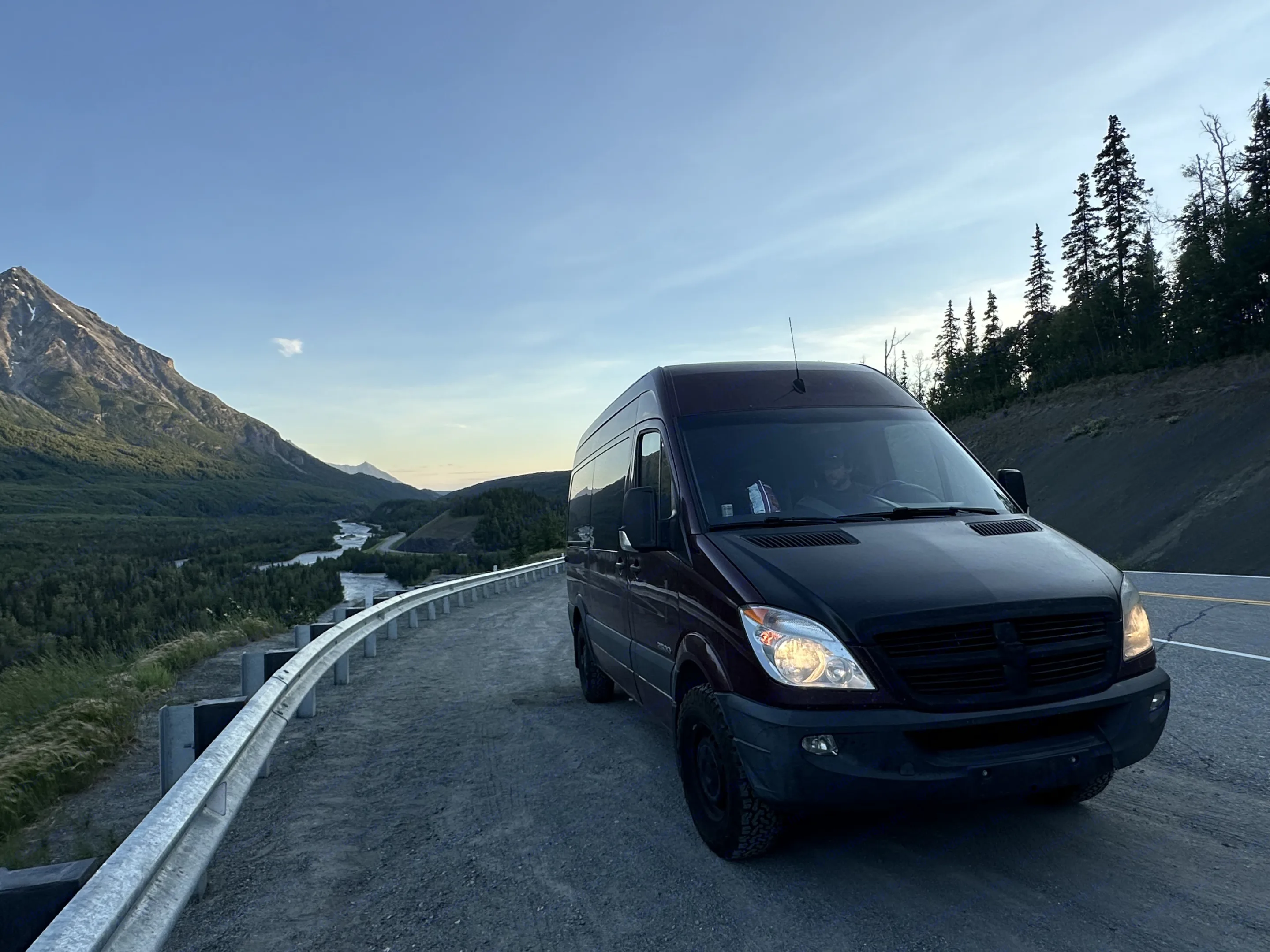 Experience nature with an rv rental! A dark camper van is parked on a mountain pass overlooking a scenic valley with a river and forests.. Dodge Sprinter Van 2008