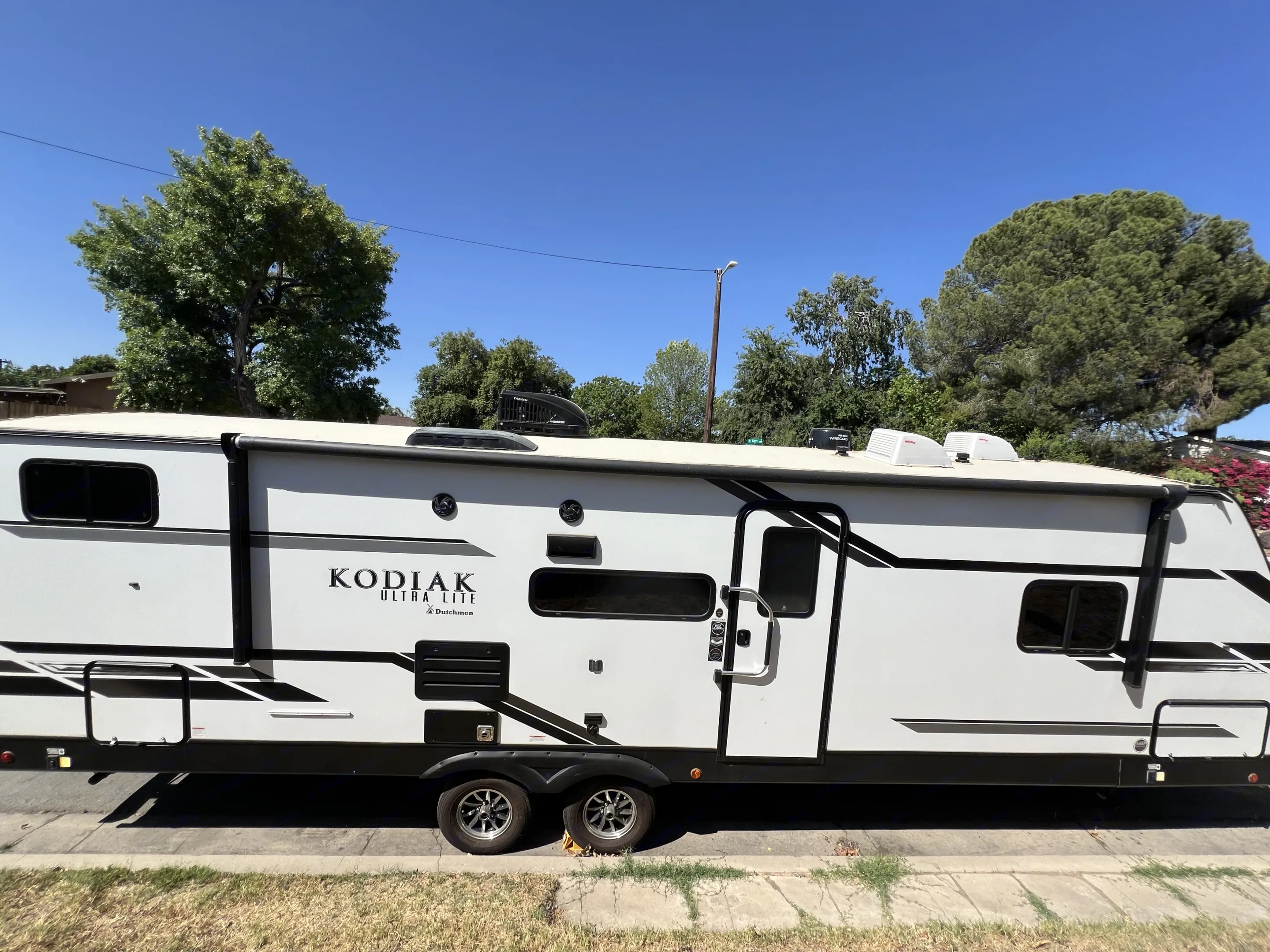 White Kodiak Ultra Lite travel trailer RV rental, parked on a street under a clear sky. Ideal for your next outdoor adventure.. Dutchmen Kodiak Ultra Lite 2021