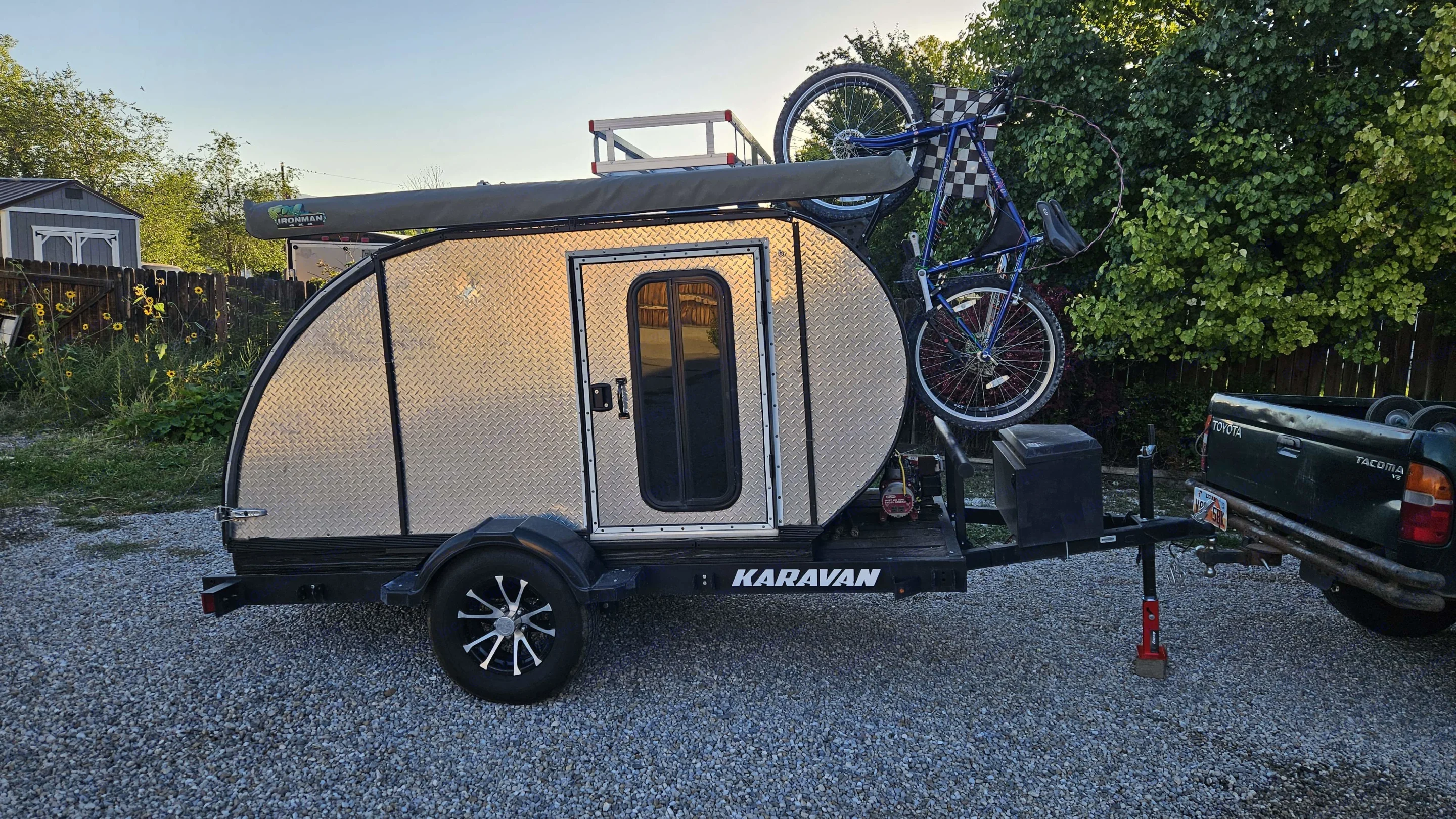 A silver teardrop camper with a bike, hitched to a truck on gravel. Perfect for your next rv. Homemade Teardrop 2020