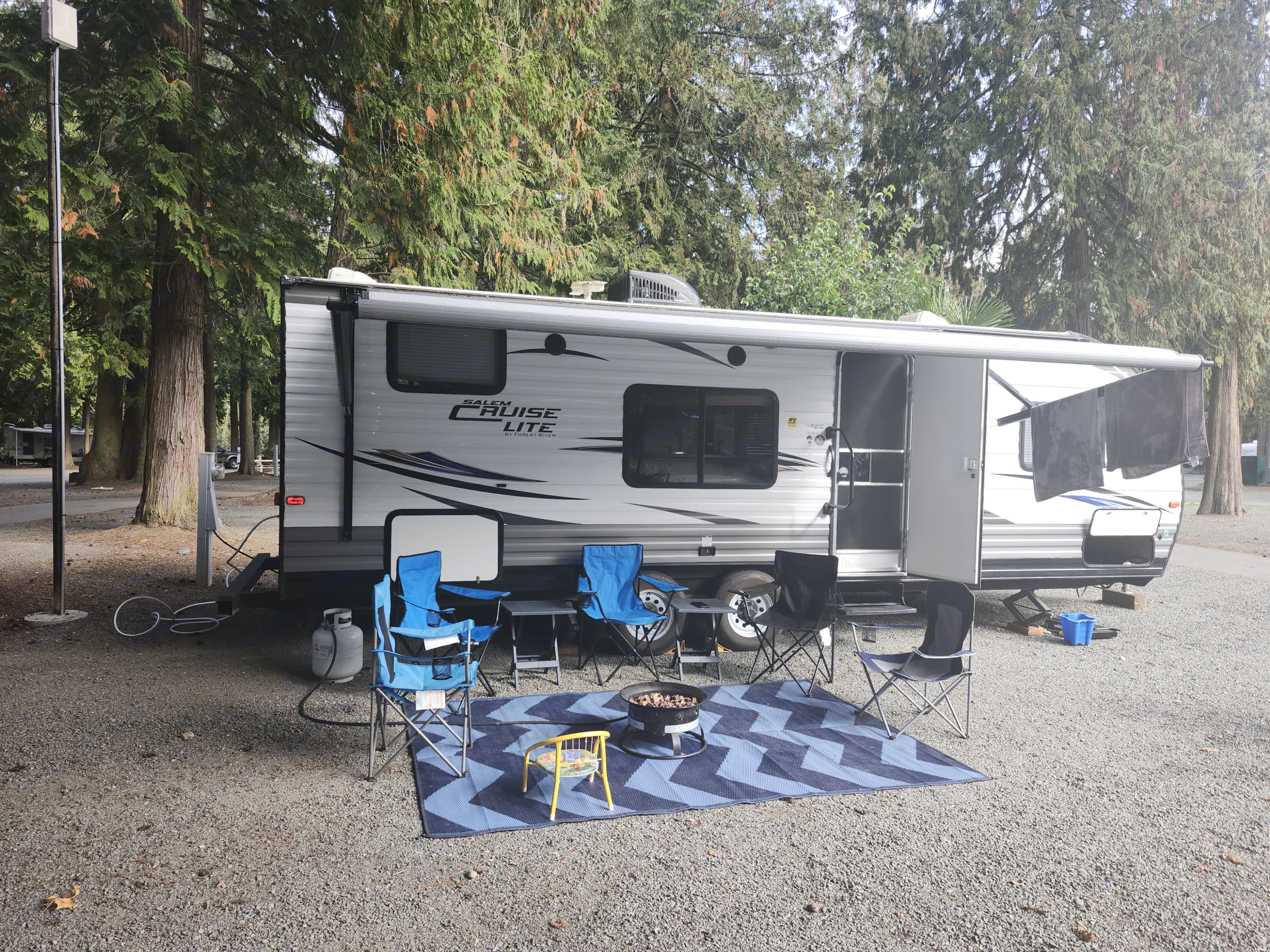 This RV rental, a Salem Cruise Lite, offers a perfect campsite with an outdoor mat, chairs, and a fire pit for a relaxing trip.. Forest River Salem Cruise Lite 2018