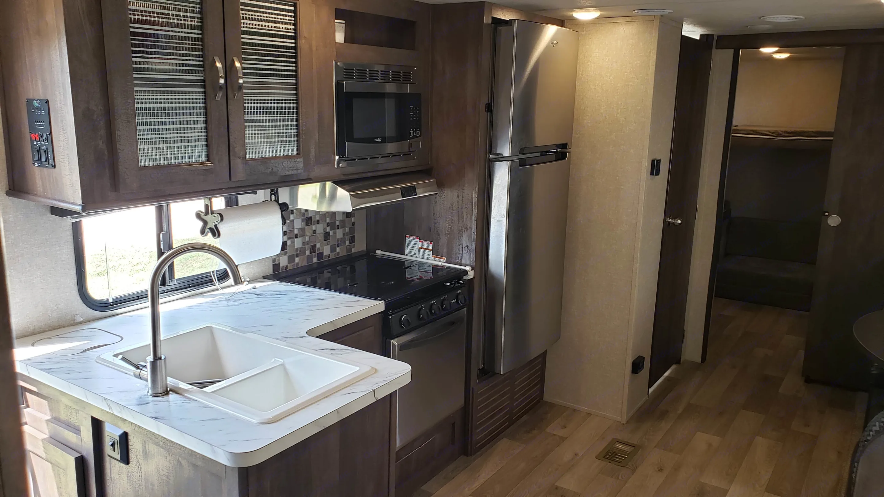 Modern RV rental interior: a fully equipped kitchen with sink, stove, microwave, and fridge, plus bunk beds visible.. Forest River Vibe 2019