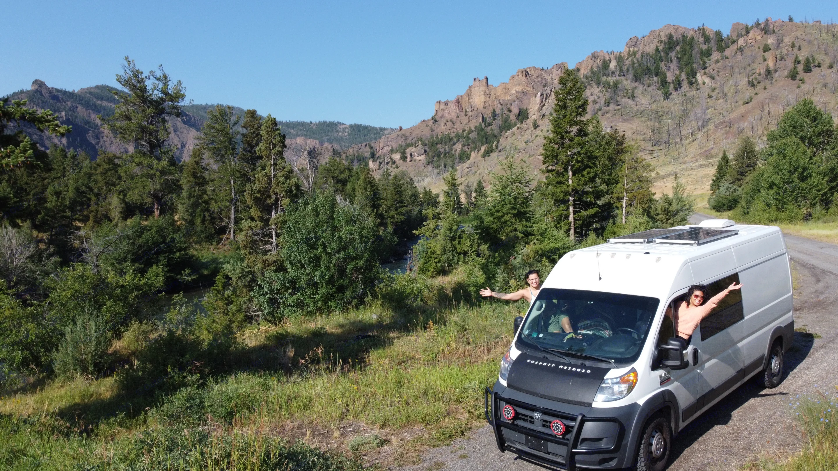 RV rental: Two smiling travelers in a white camper van on a mountain road by a river, solar panels visible.. Dodge Promaster 2500 2017