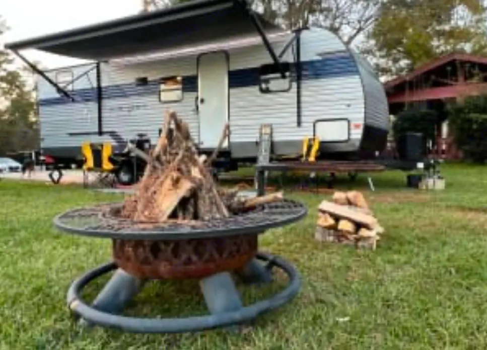 RV rental travel trailer and fire pit with wood, ready for an outdoor camping adventure on the grass.. Avenger LE 2022